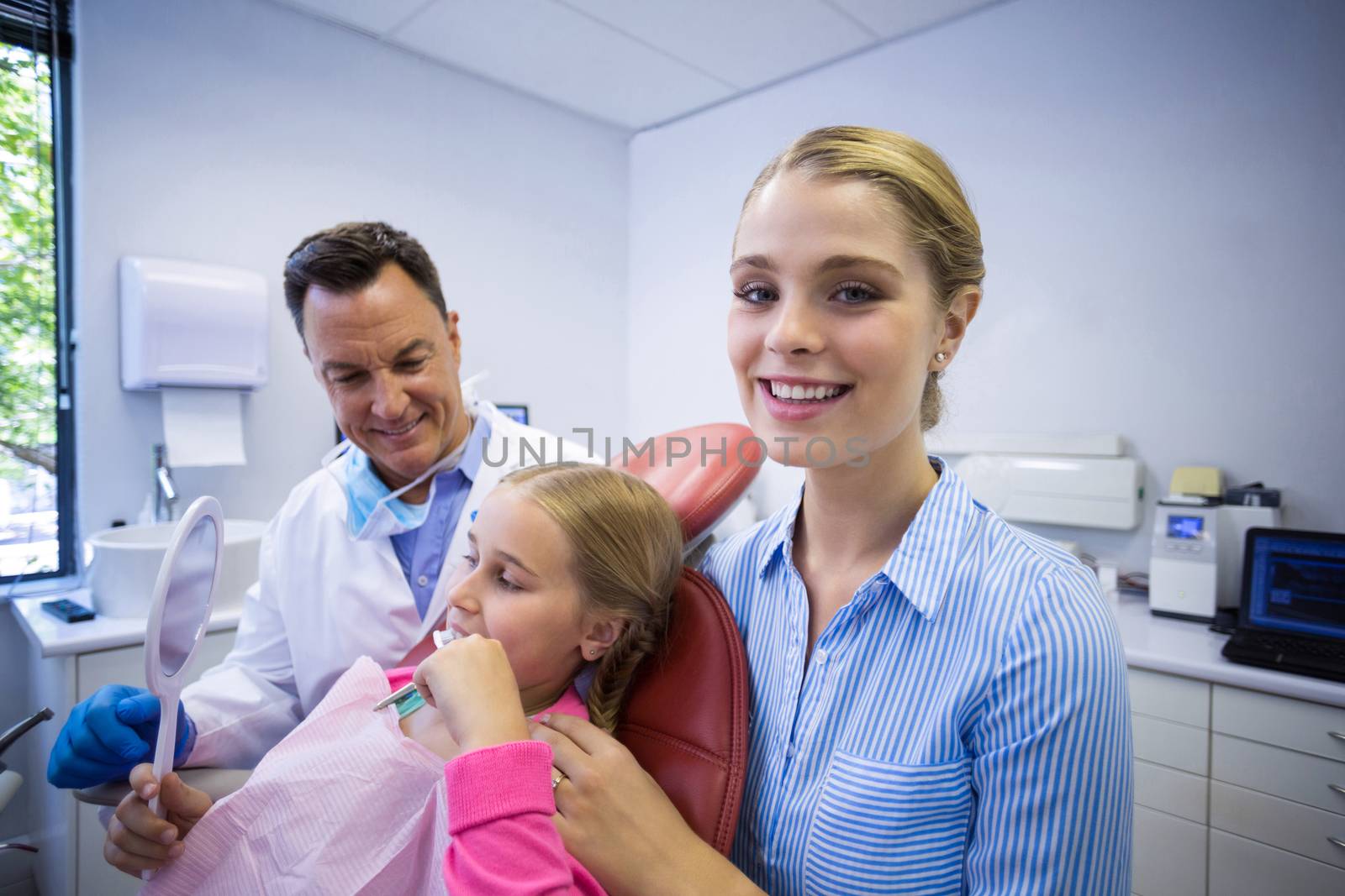 Dentist assisting young patient while brushing teeth in dental clinic