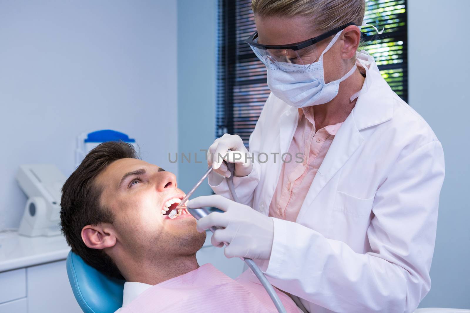 Dentist holding medical equipment while giving treatment to patient by Wavebreakmedia