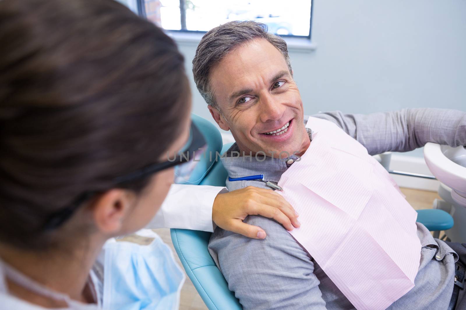 Happy patient looking at dentist while sitting on chair in clinic