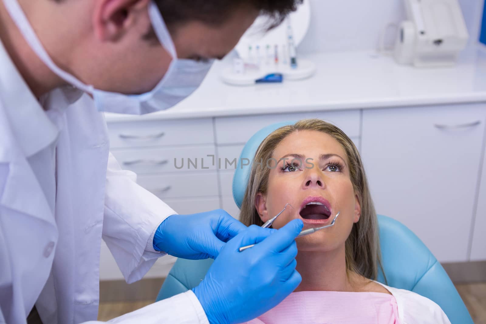 Dentist holding tools while examining woman at medical clinic by Wavebreakmedia
