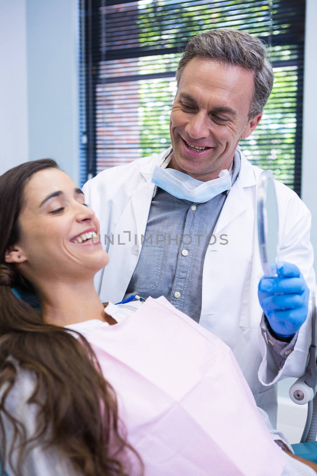 Happy dentist showing mirror to patient at medical clinic