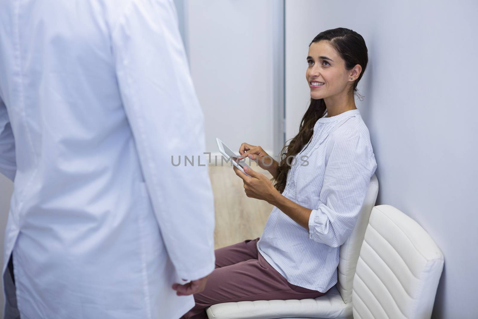 Side view of woman holding tablet while looking at dentist in clinic