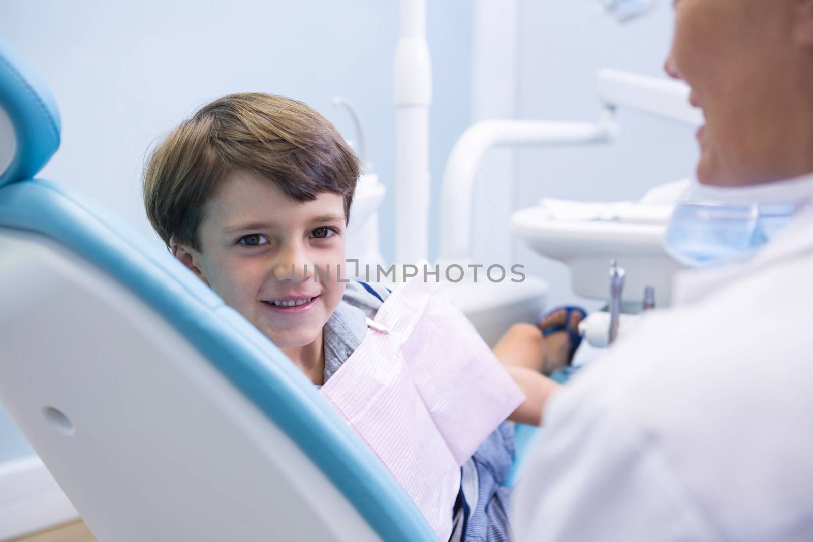 Portrait of cute boy sitting on dentist chair by dentist at medical clinic