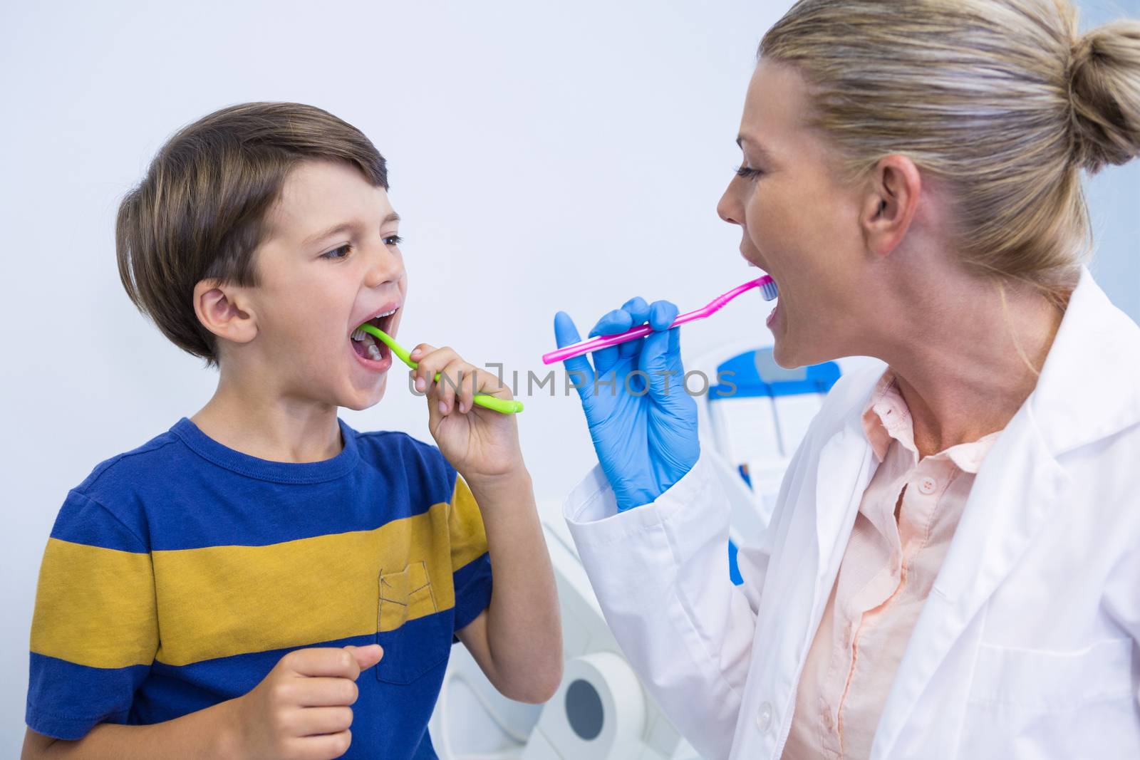 Dentist and boy brushing teeth against wall at clinic 