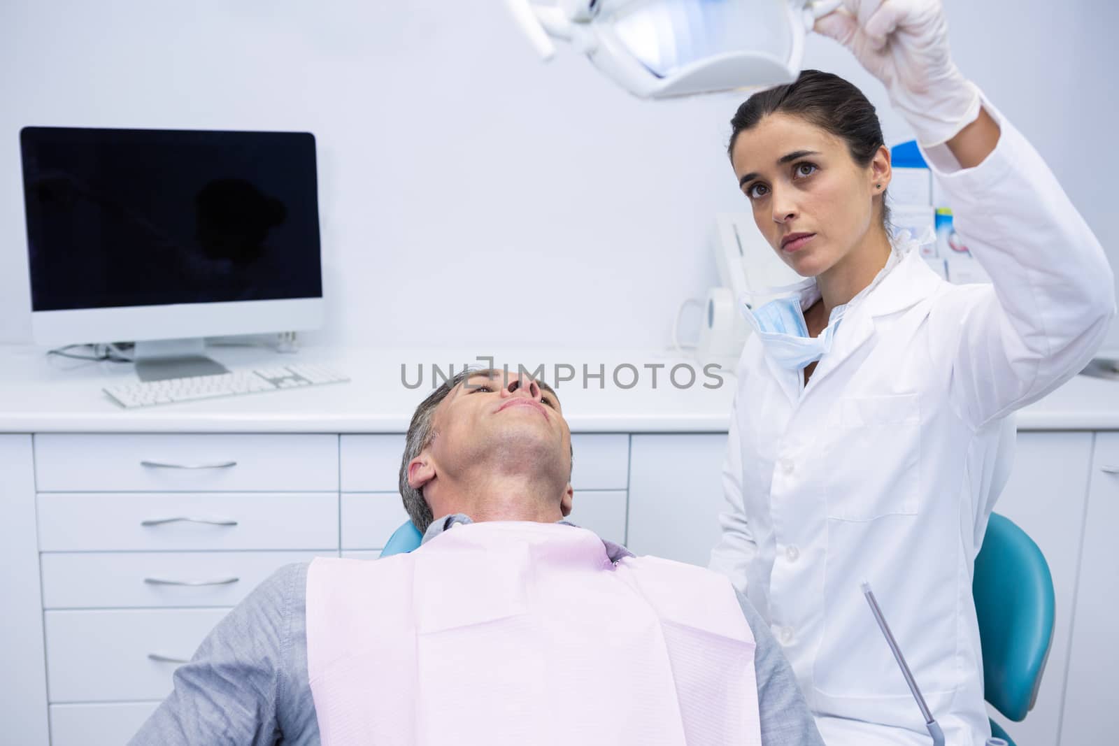 Dentist adjusting electric light while patient sitting on chair at dental clinic