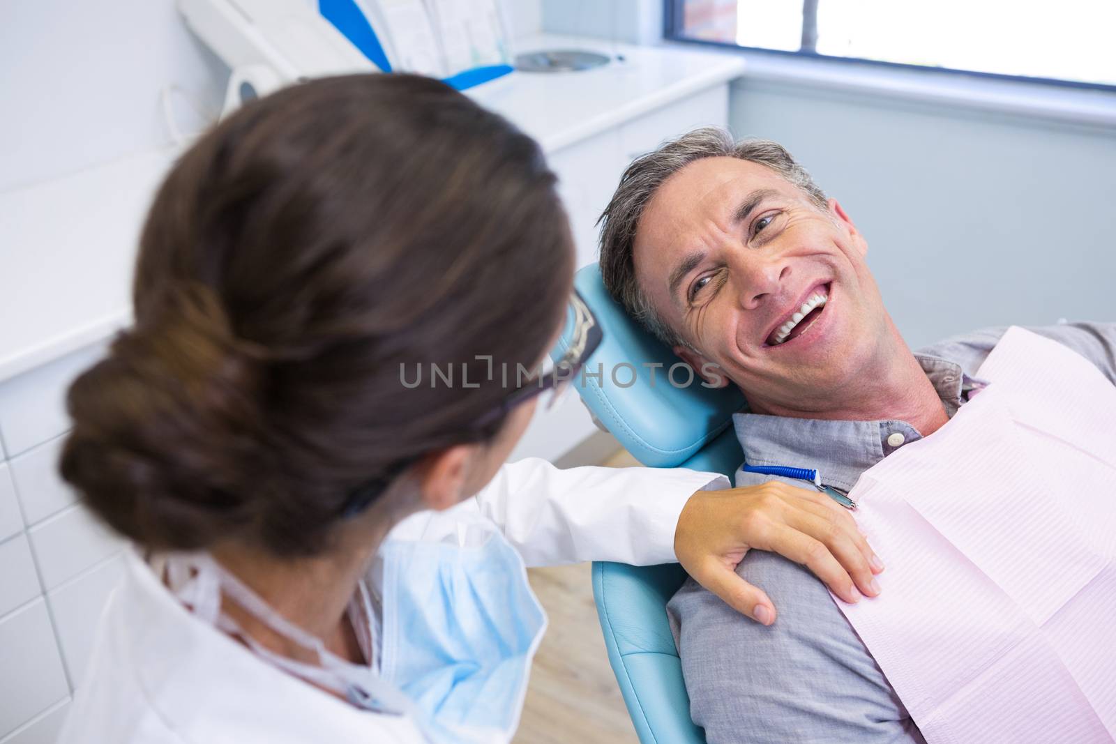 Patient sitting on chair while looking at dentist in medical clinic by Wavebreakmedia