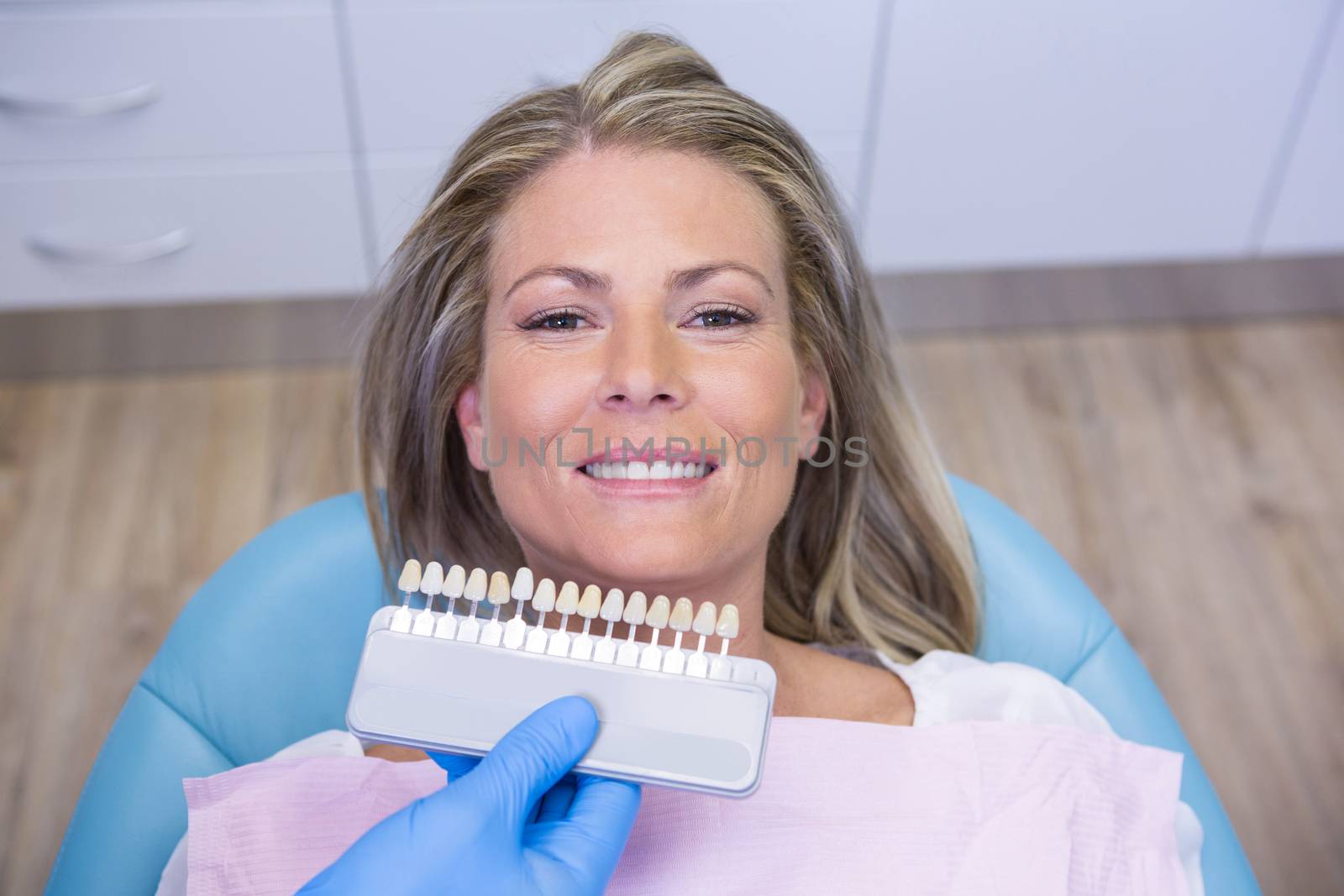 High angle view of dentist holding tooth whitening equipment by smiling patient at clinic