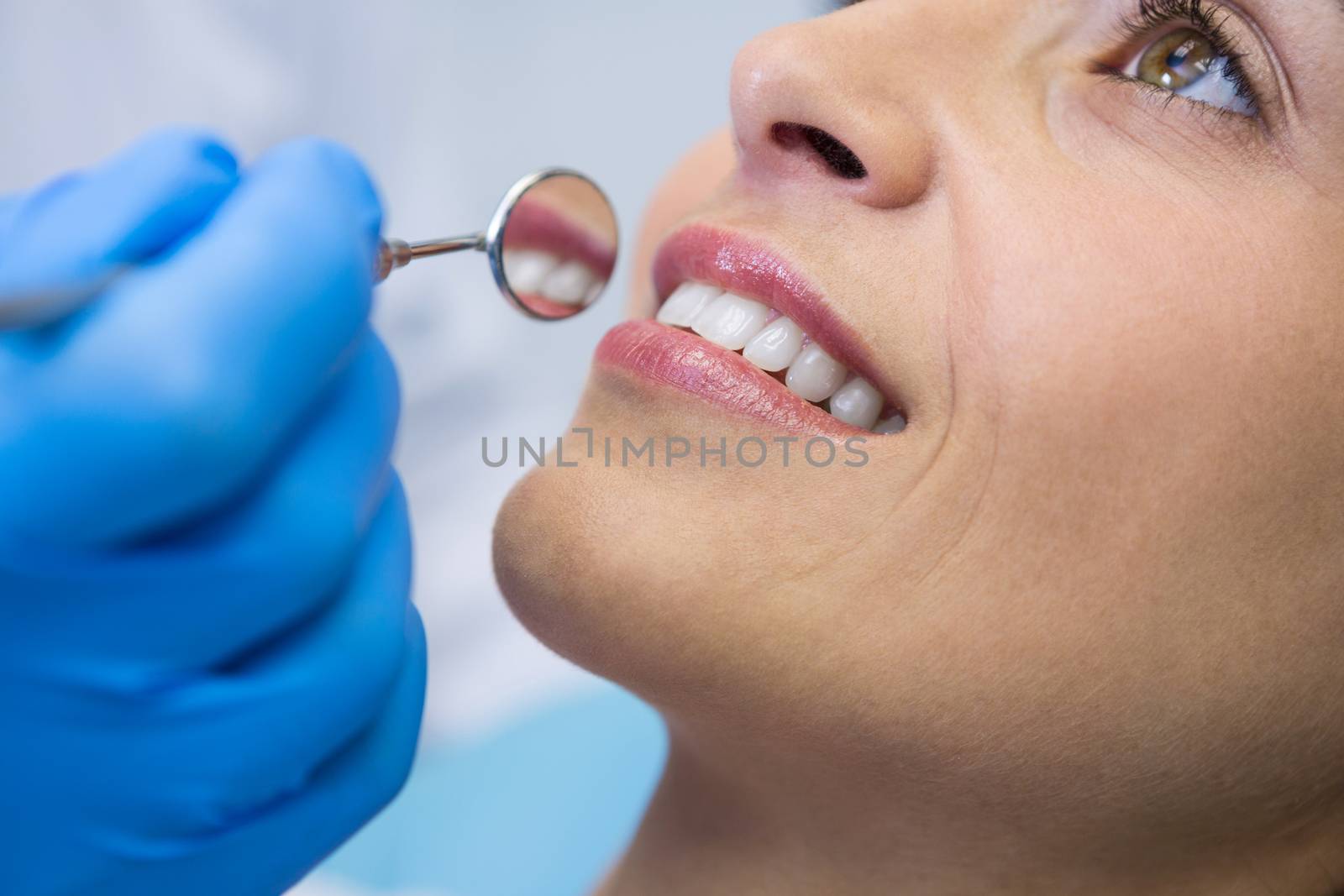Dentist holding angled mirror by smiling woman at clinic by Wavebreakmedia