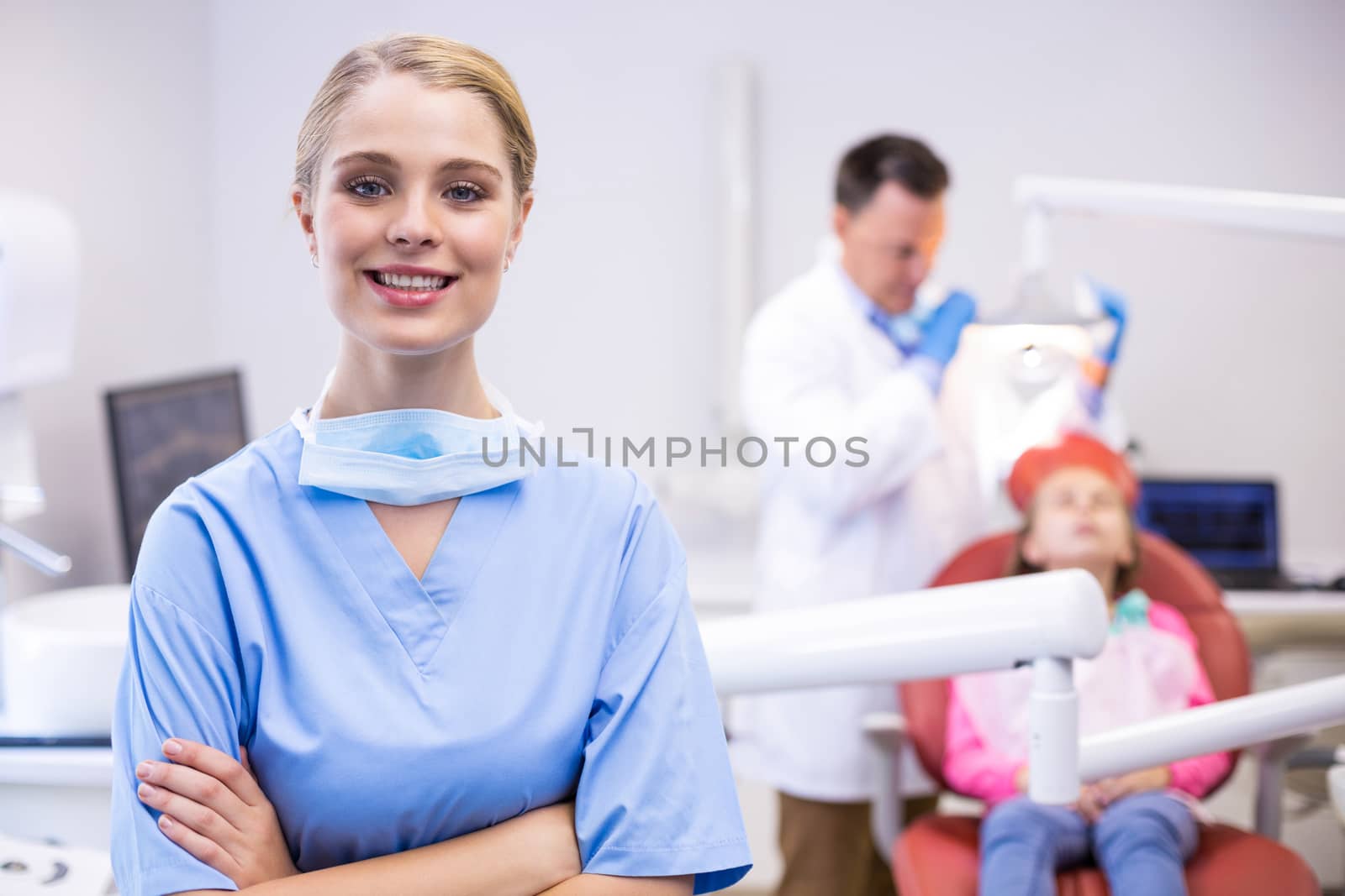 Portrait of smiling nurse with arms crossed while dentist examining patient in background