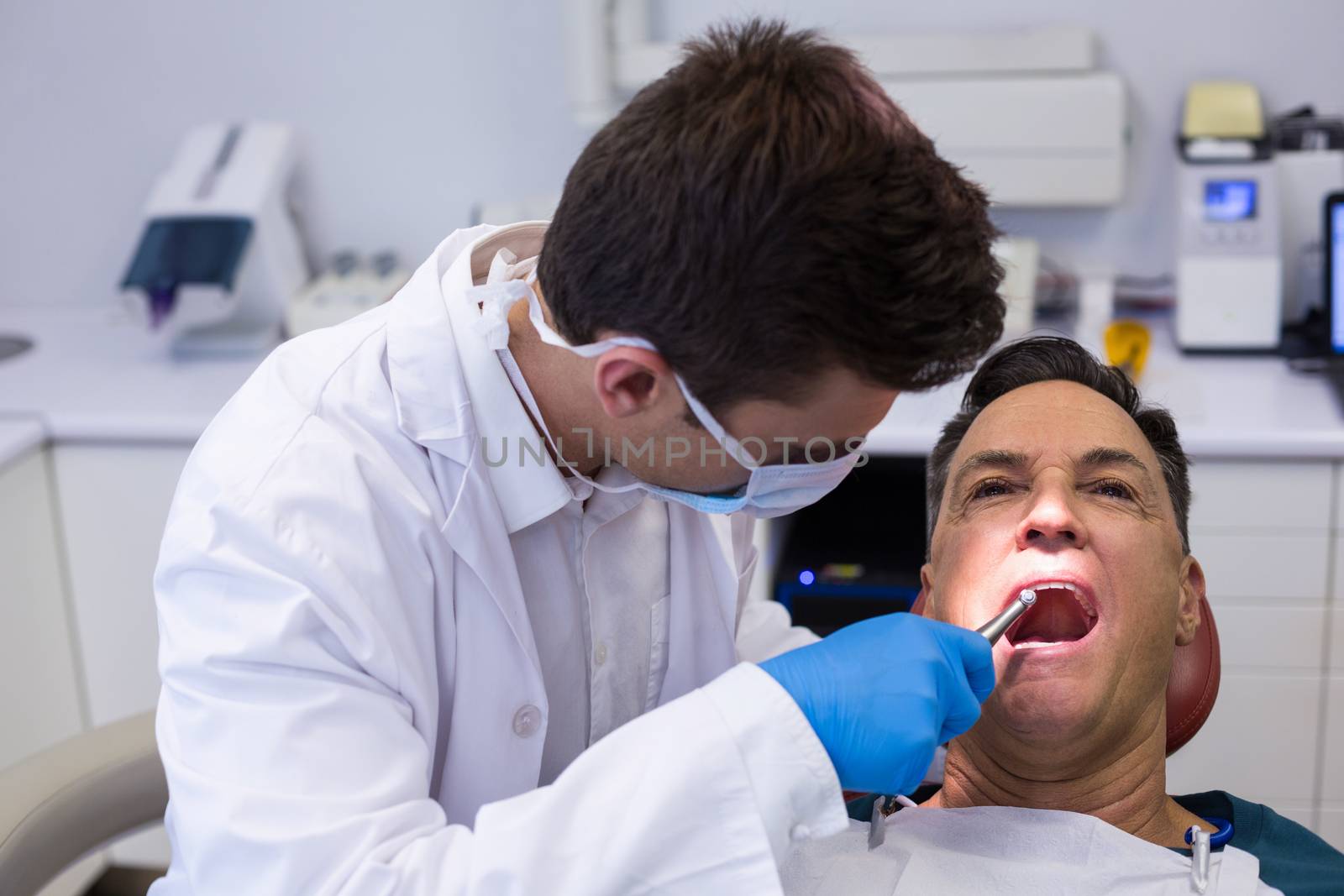 Dentist examining a male patient with tools in clinic