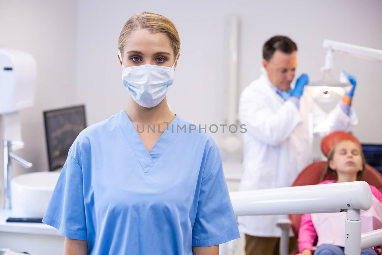 Portrait of female nurse wearing surgical mask while dentist examining patient in background