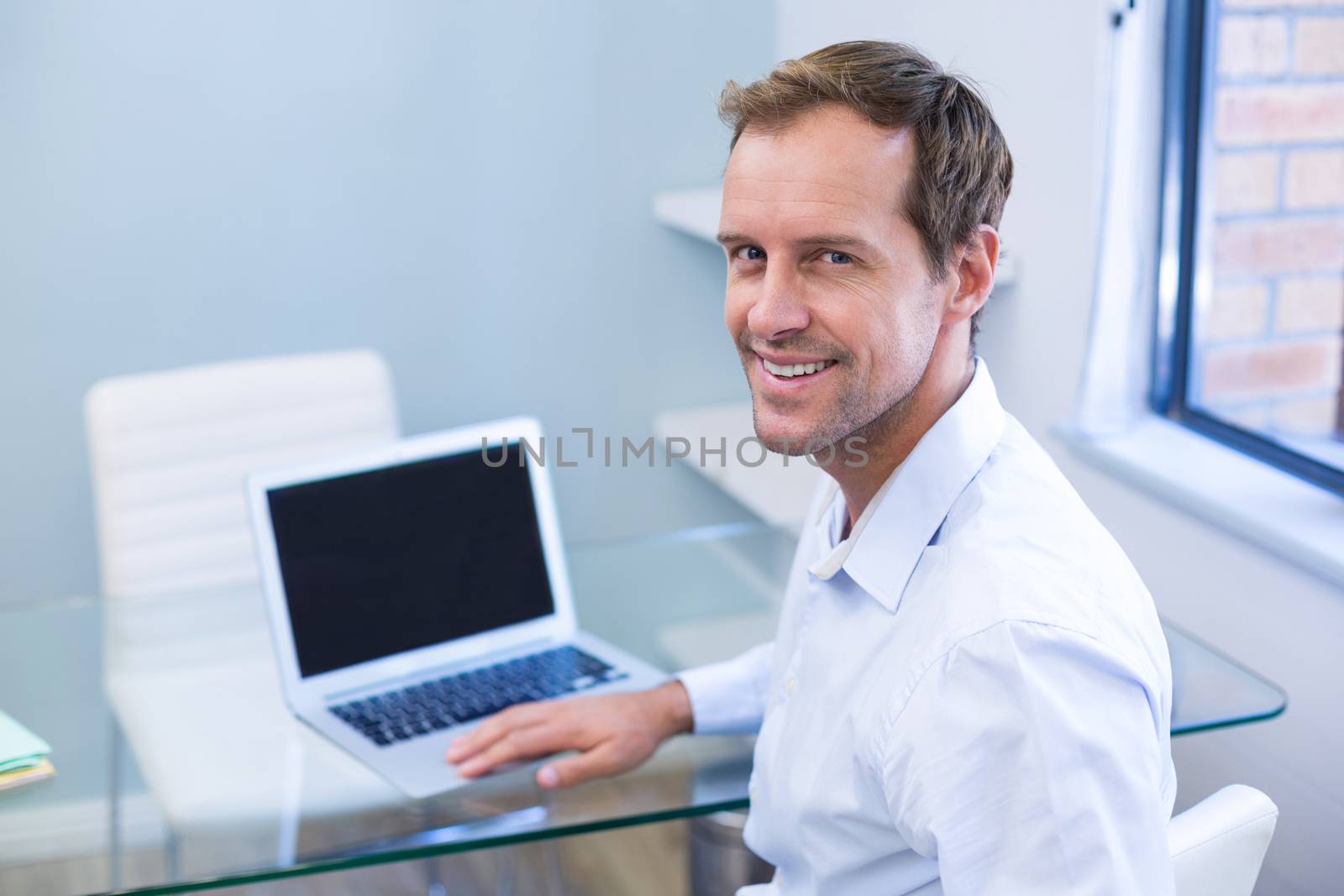 Portrait of smiling dentist working on laptop in dental clinic
