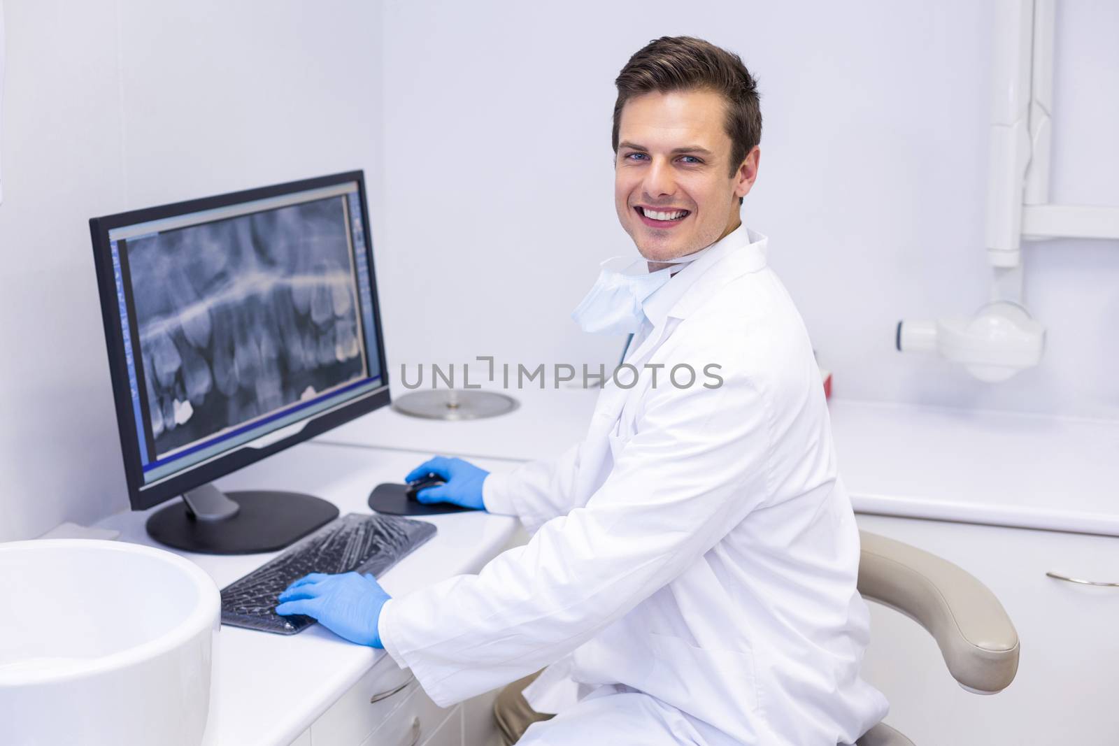 Portrait of happy dentist examining x-ray report on computer by Wavebreakmedia