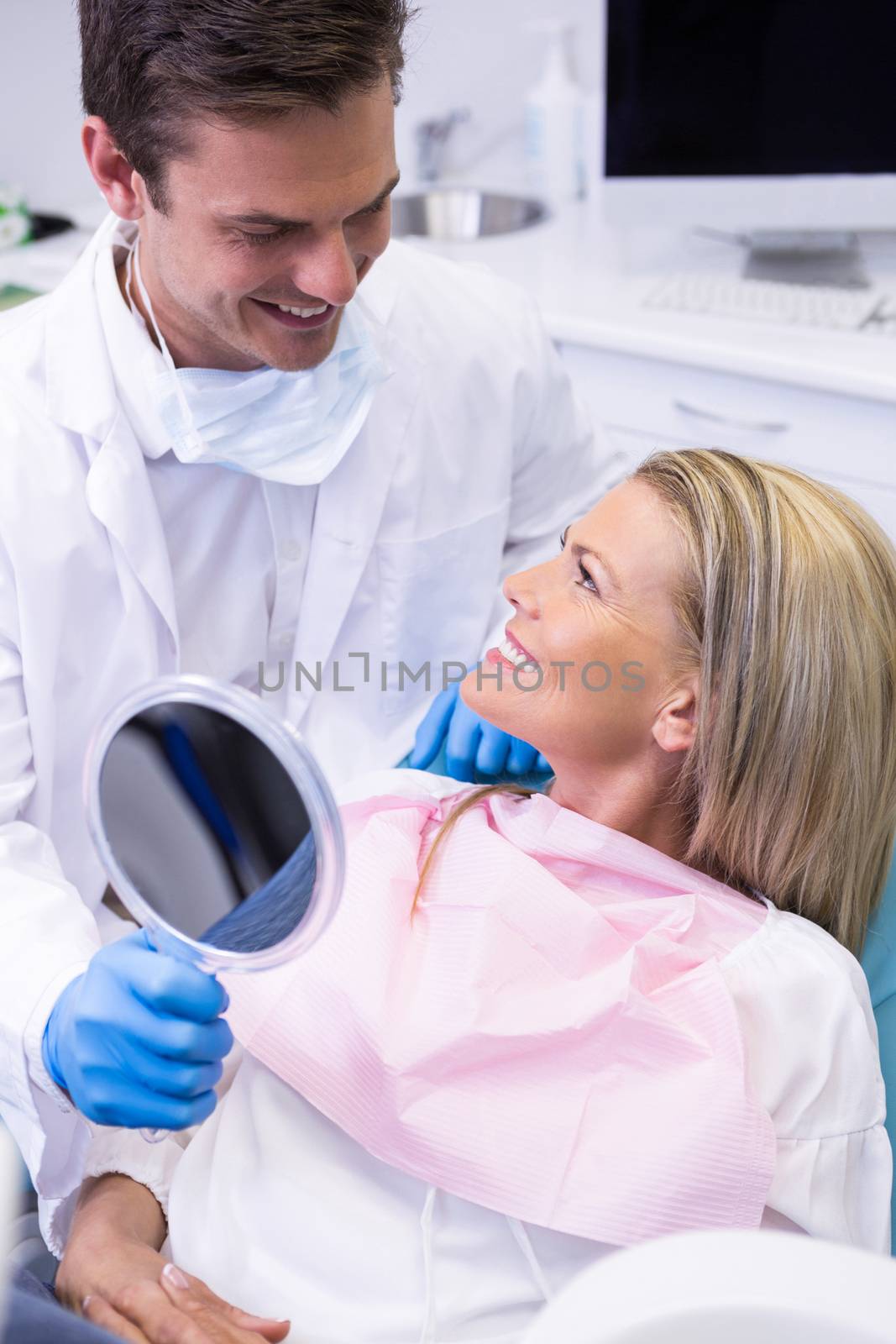 Dentist showing mirror to happy patient at dental clinic