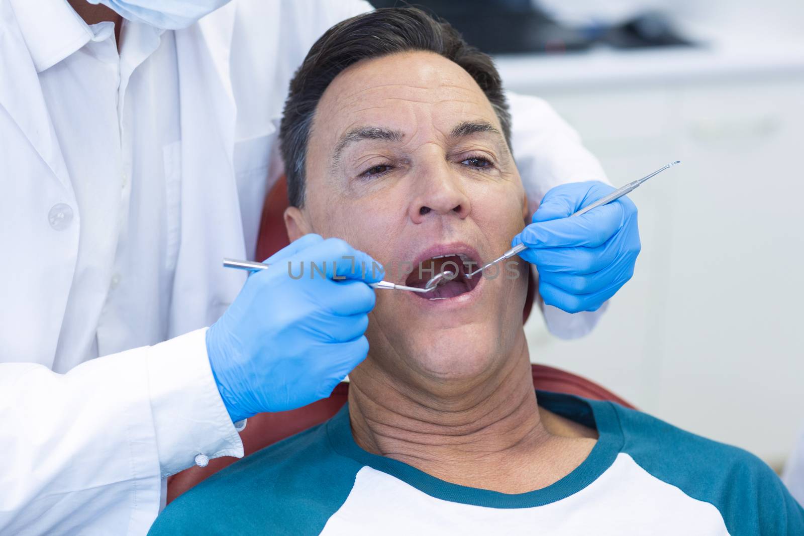 Dentist examining a male patient with tools by Wavebreakmedia