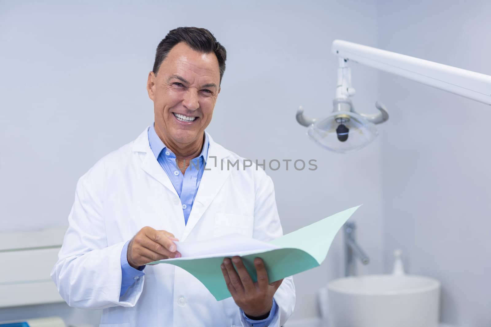 Portrait of smiling dentist holding file in dental clinic