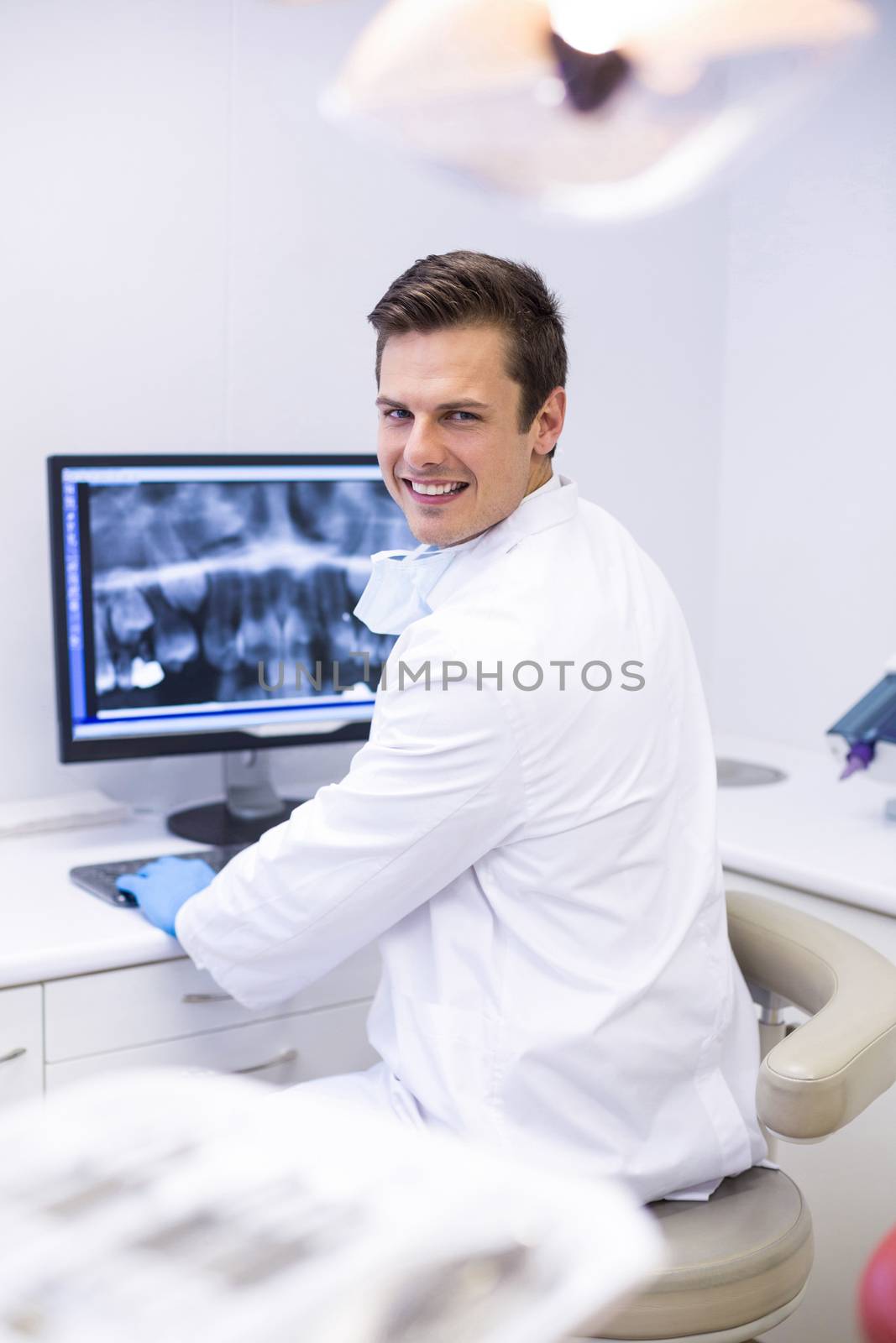 Portrait of happy dentist examining x-ray report on computer by Wavebreakmedia