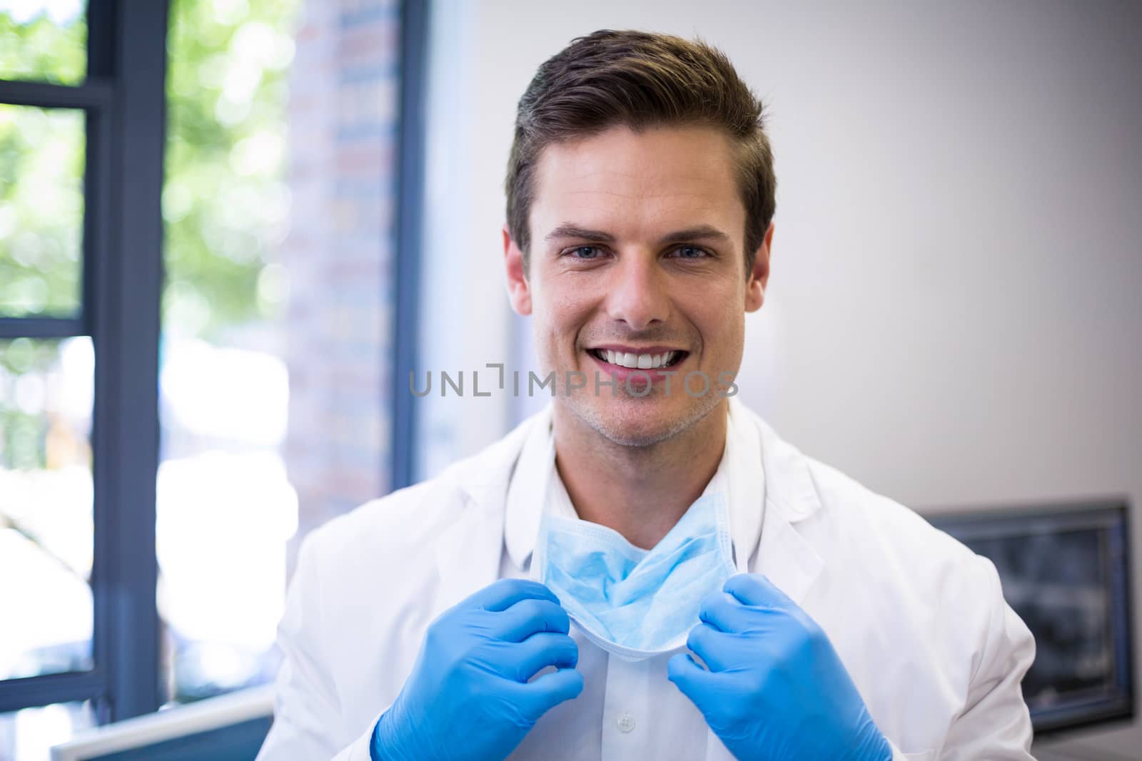 Portrait of happy dentist holding surgical mask by Wavebreakmedia