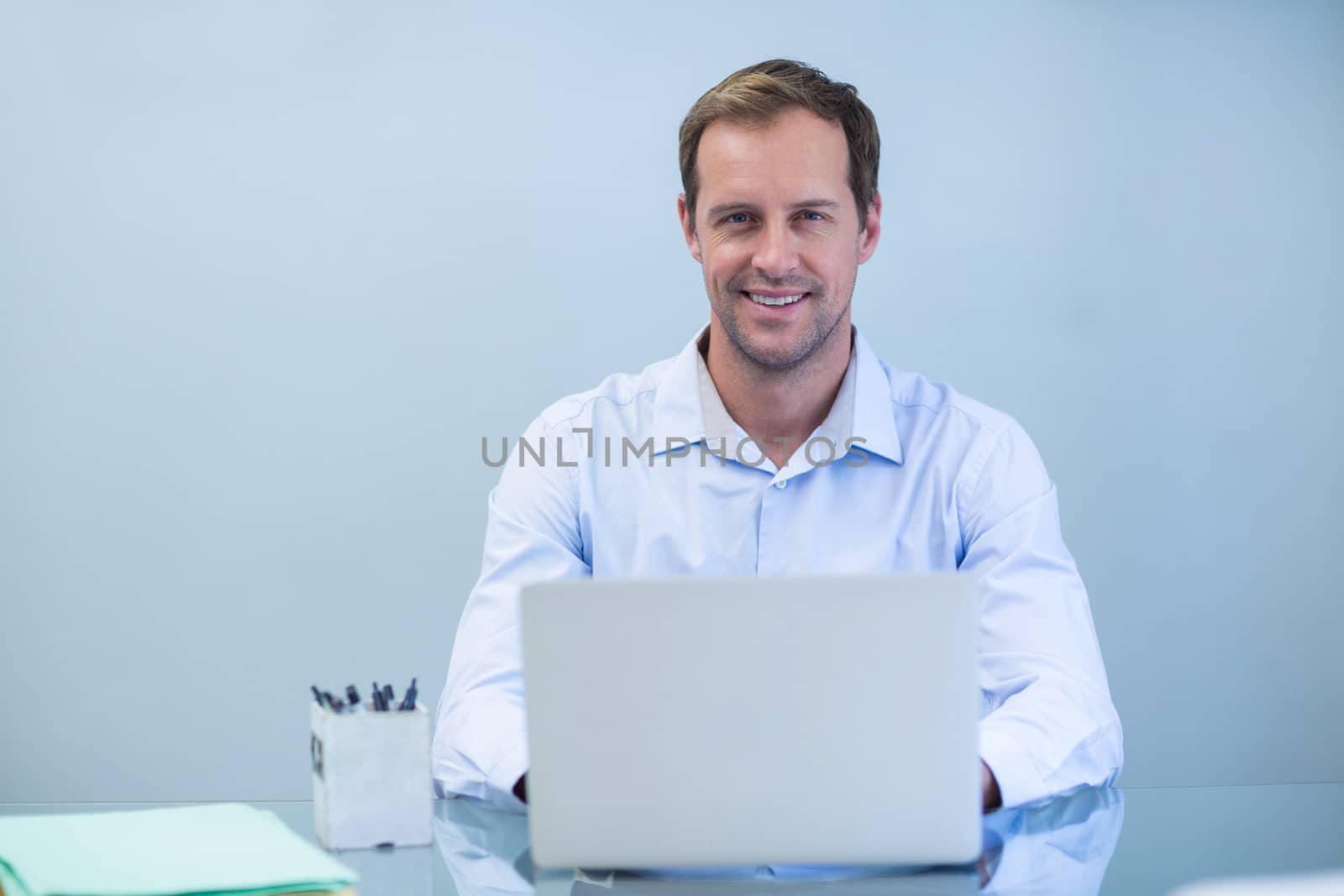 Portrait of smiling dentist working on laptop in dental clinic