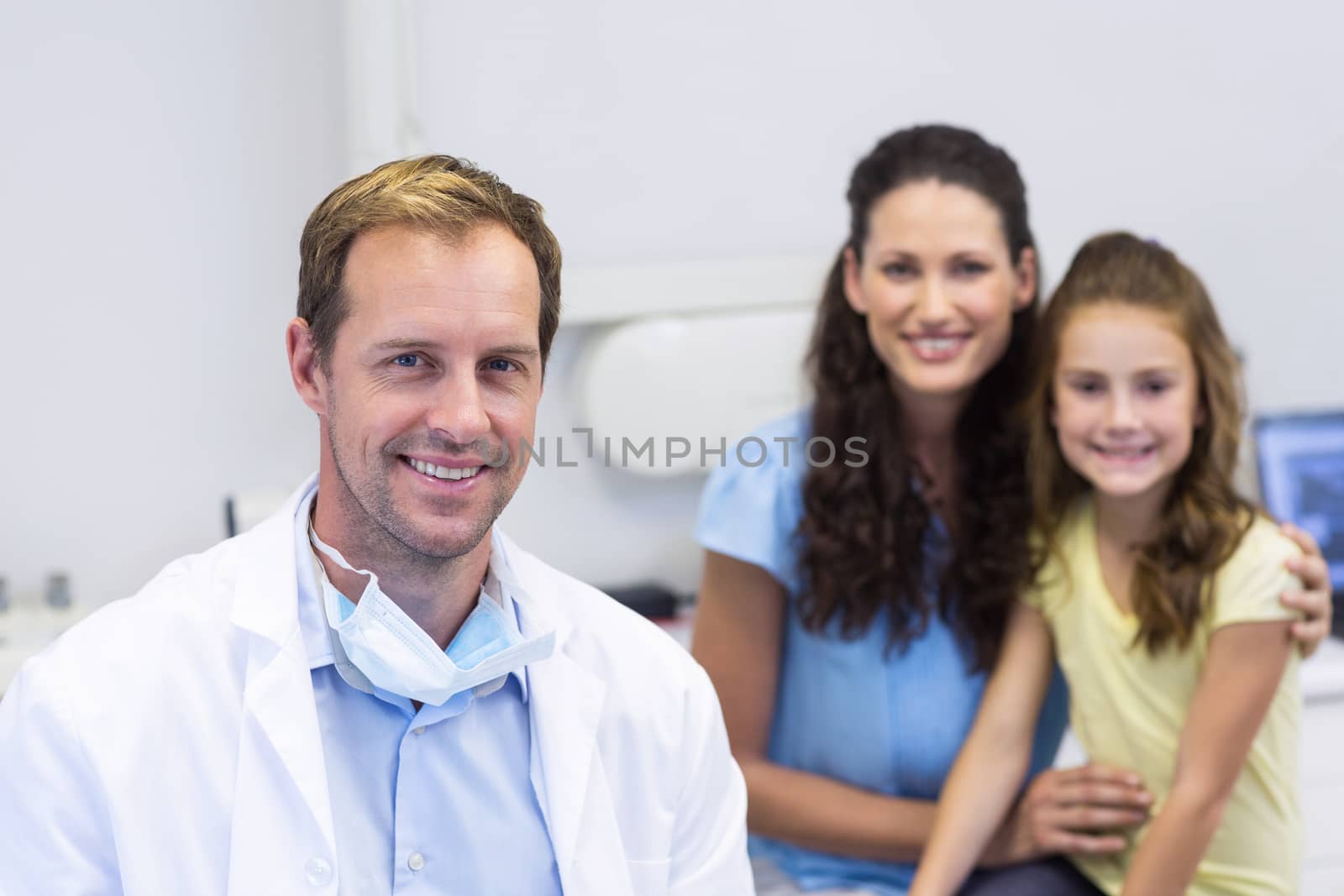 Portrait of dentist with young patient and her mother at dental clinic