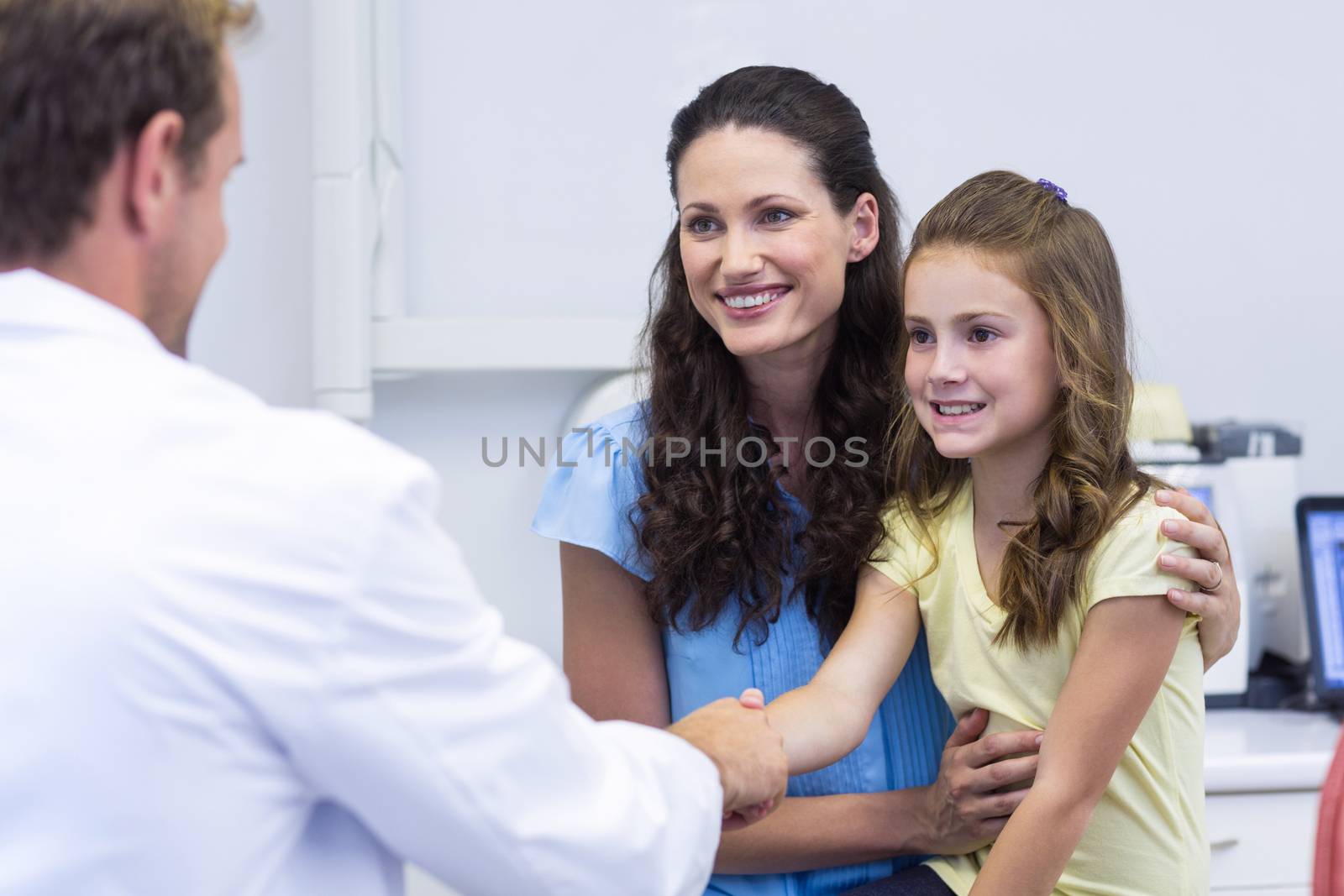Dentist shaking hand with daughter after dental examination by Wavebreakmedia