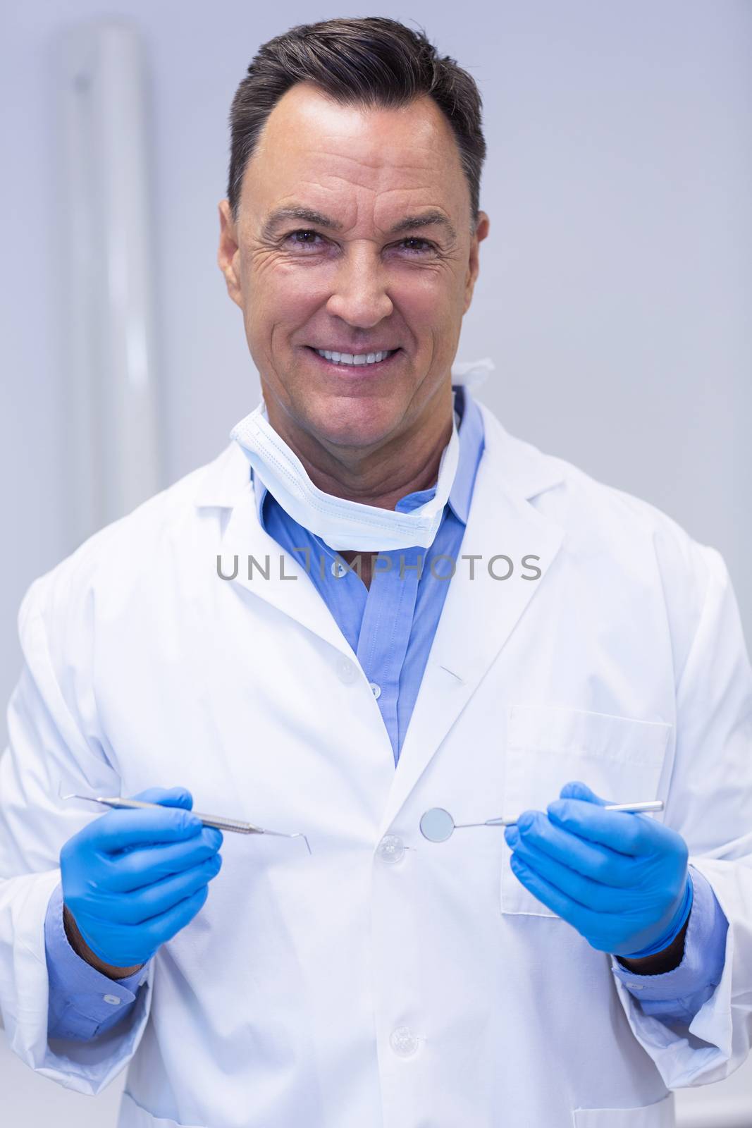 Portrait of smiling dentist holding dental tools by Wavebreakmedia