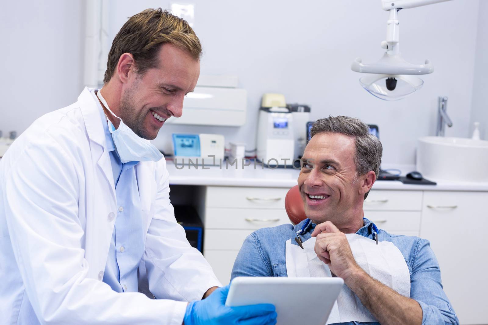 Dentist discussing over digital tablet with male patient in dental clinic