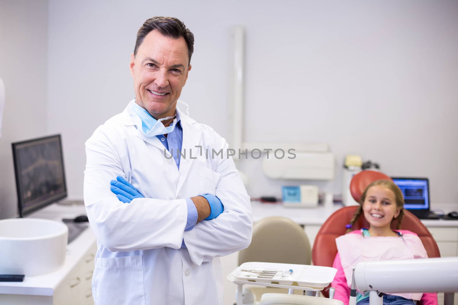 Smiling dentist standing with arms crossed at dental clinic by Wavebreakmedia