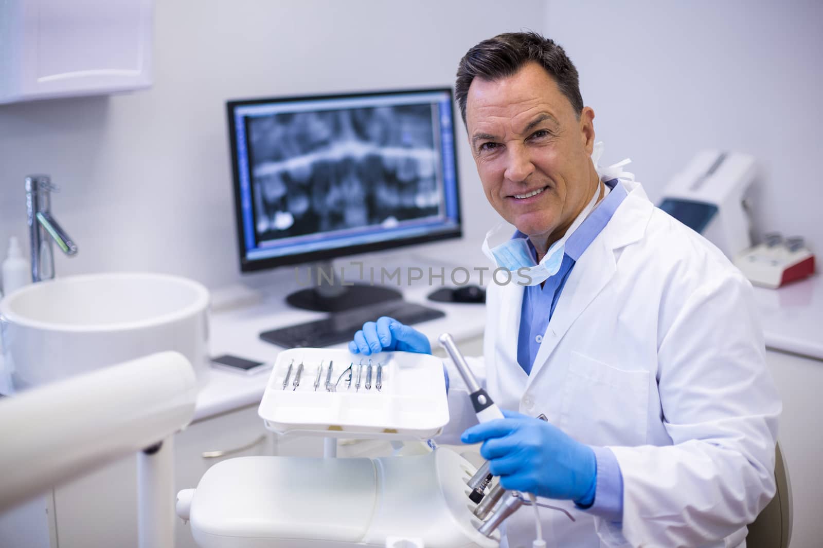 Portrait of smiling dentist holding dental hand piece in clinic