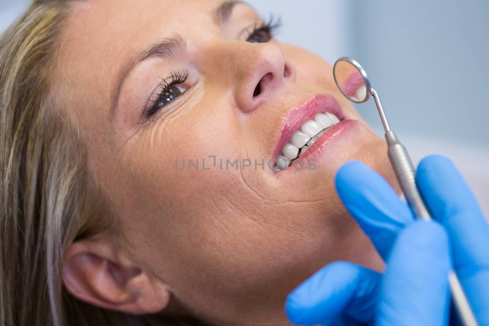 Dentist holding angled mirror by woman at medical clinic by Wavebreakmedia