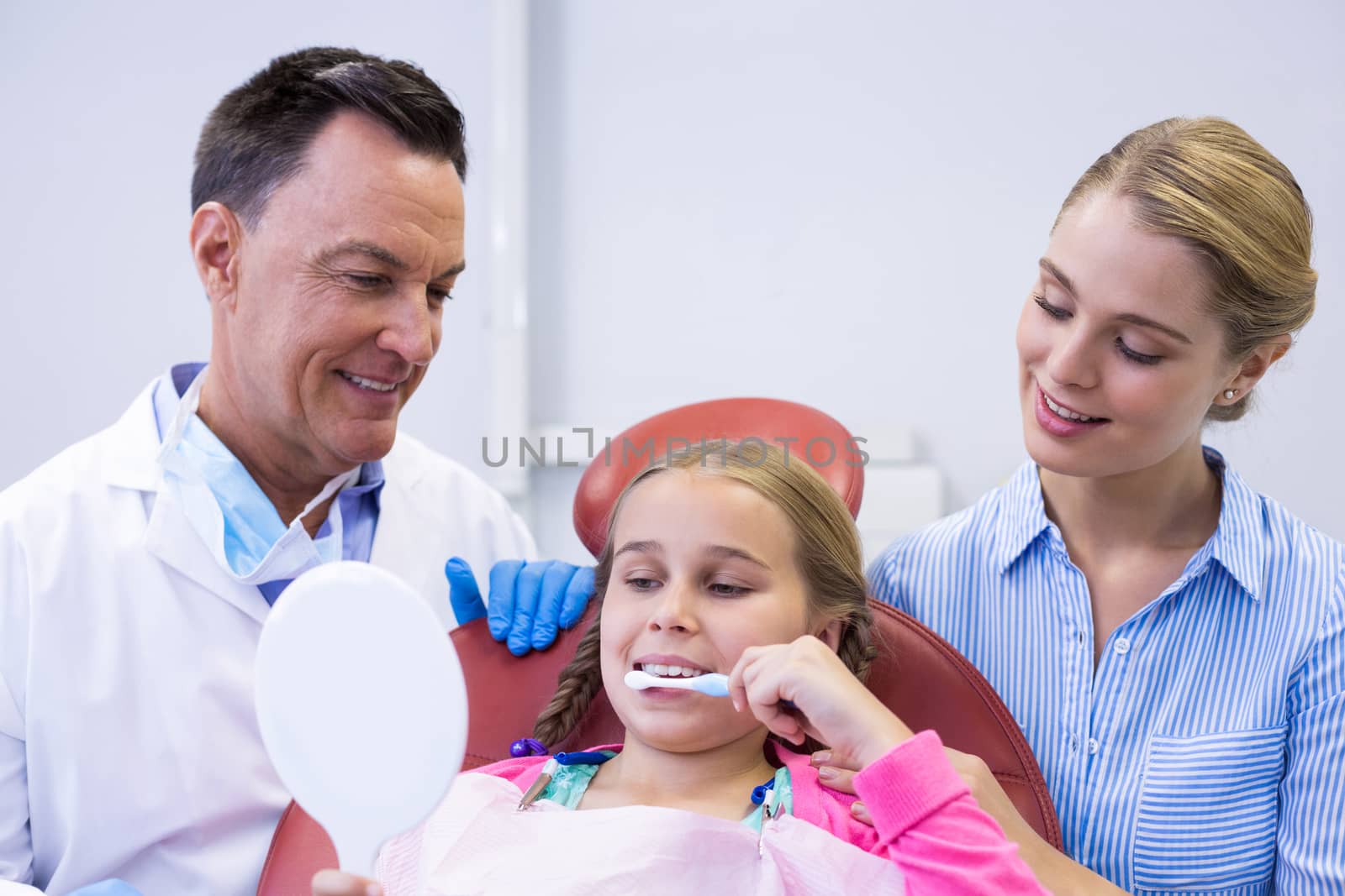 Dentist assisting young patient while brushing teeth in dental clinic