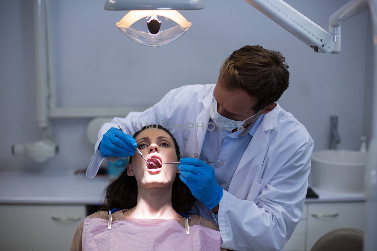 Dentist examining a female patient with tools by Wavebreakmedia