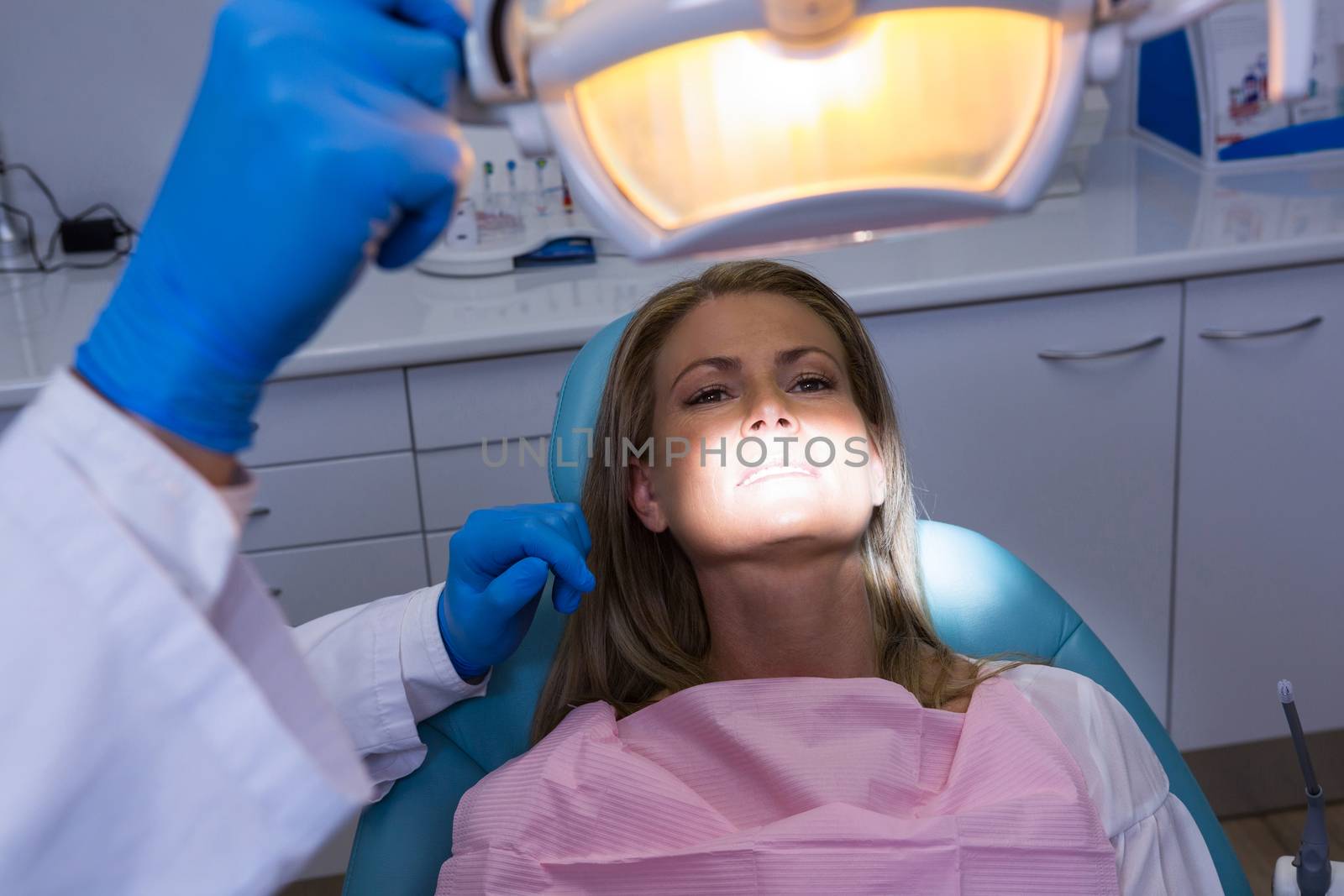 Woman lying on dentist chair while dentist adjusting electric lamp by Wavebreakmedia