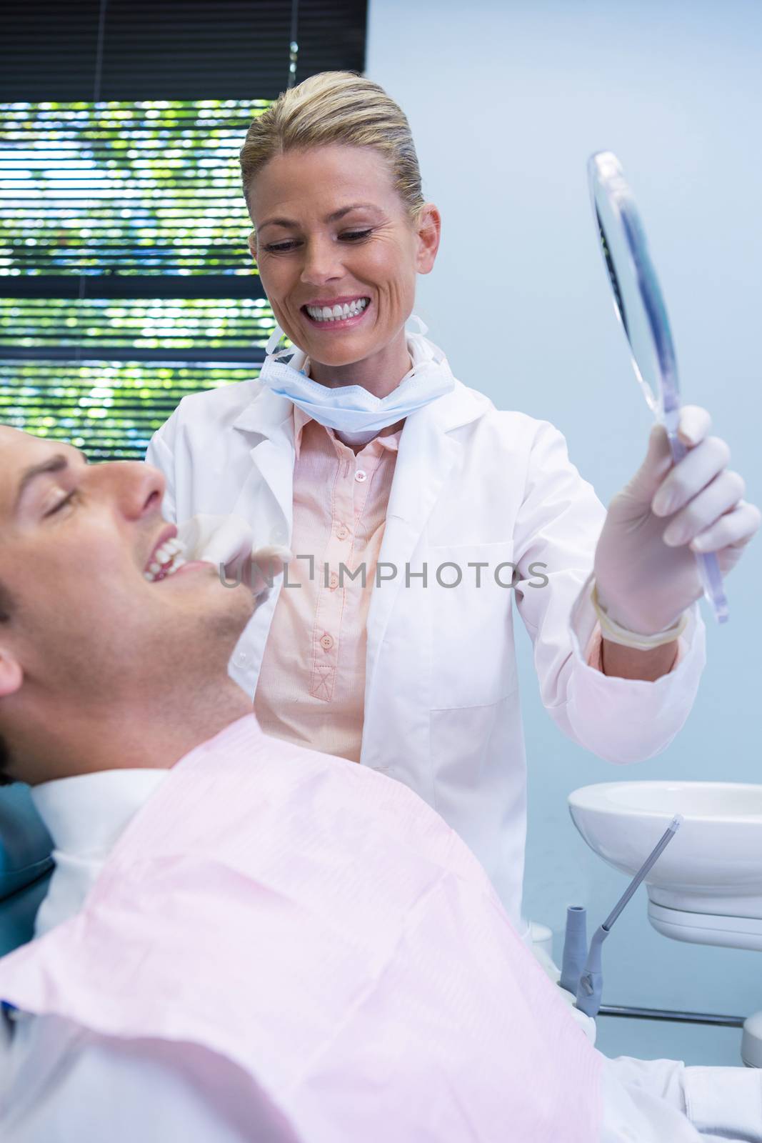 Dentist showing mirrior to patient by Wavebreakmedia