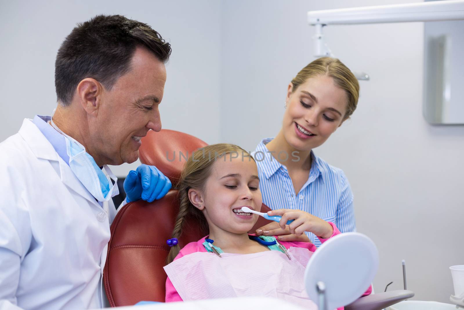 Dentist assisting young patient while brushing teeth by Wavebreakmedia