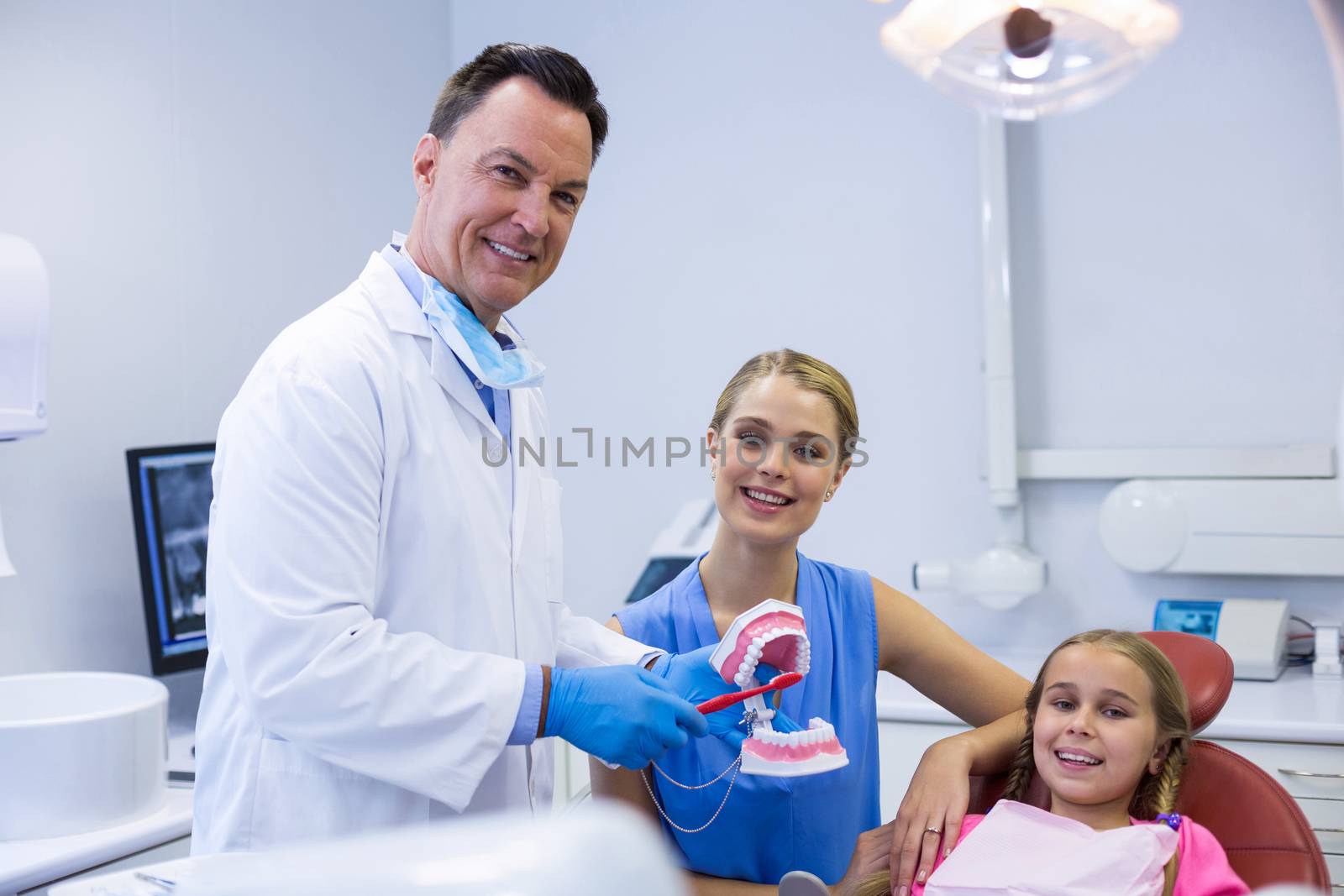 Dentist showing young patient how to brush teeth in dental clinic