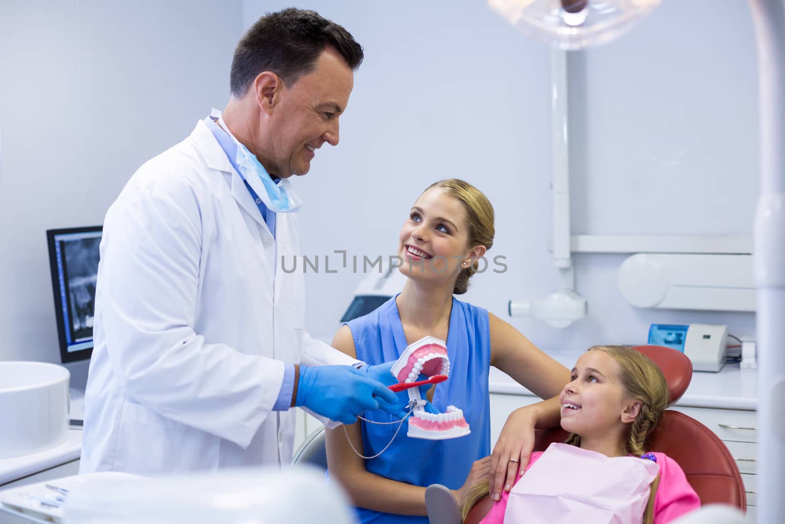 Dentist showing young patient how to brush teeth by Wavebreakmedia