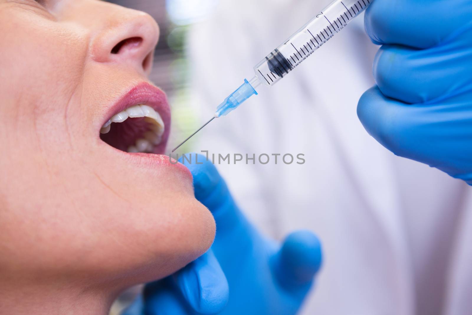 Dentist holding syringe by patient at medical clinic by Wavebreakmedia