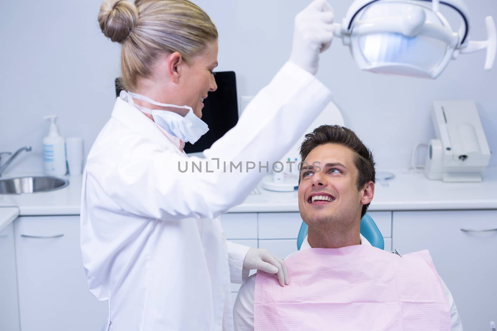 Side view of dentist adjusting electric light while patient sitting on chair at clinic