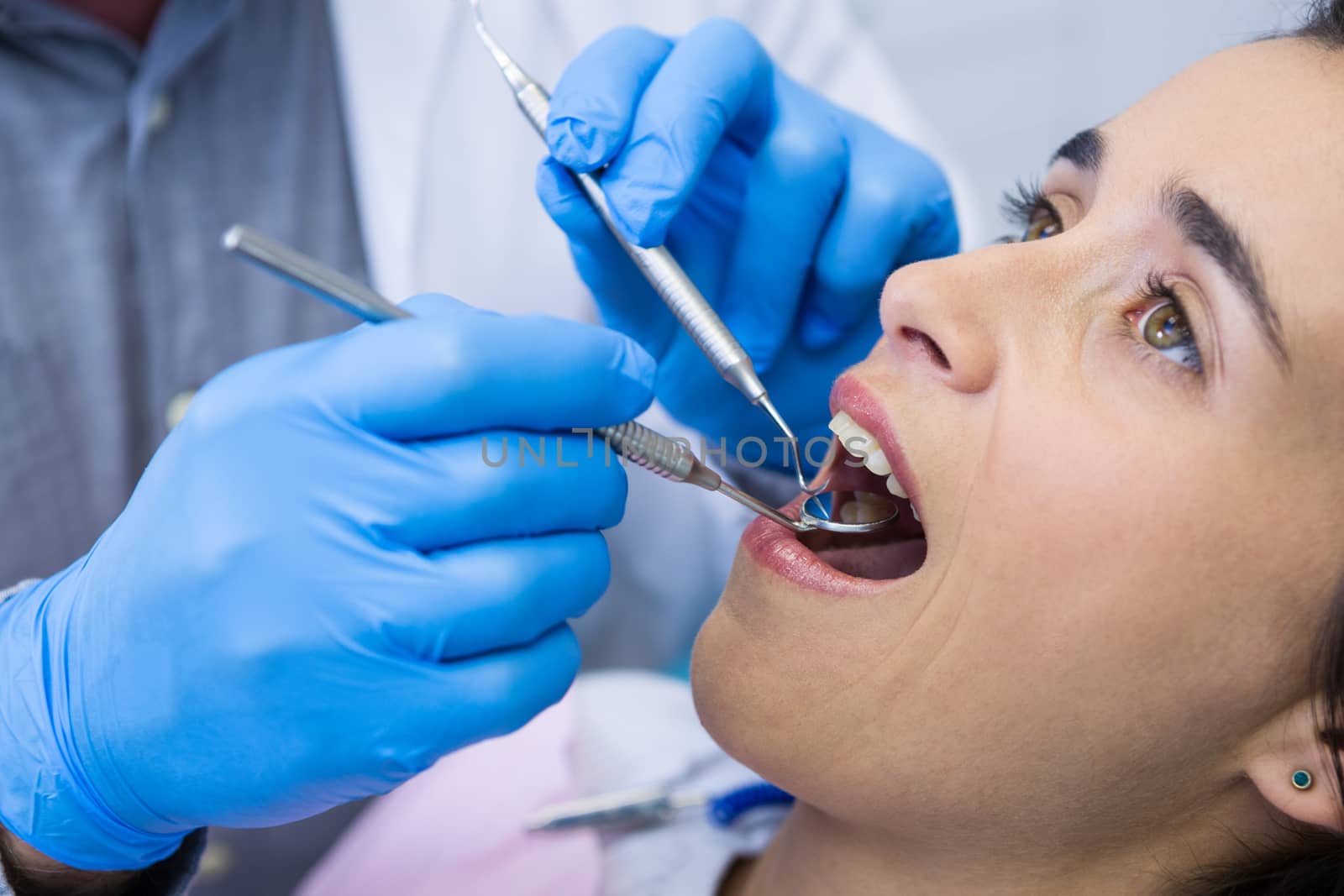 Dentist holding tools while examining woman at clinic by Wavebreakmedia