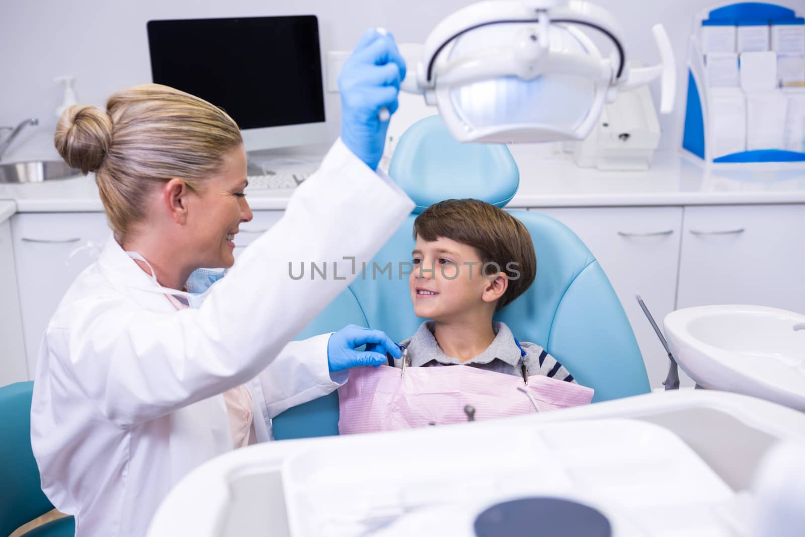 Side view of dentist adjusting electric light while boy sitting on chair by Wavebreakmedia