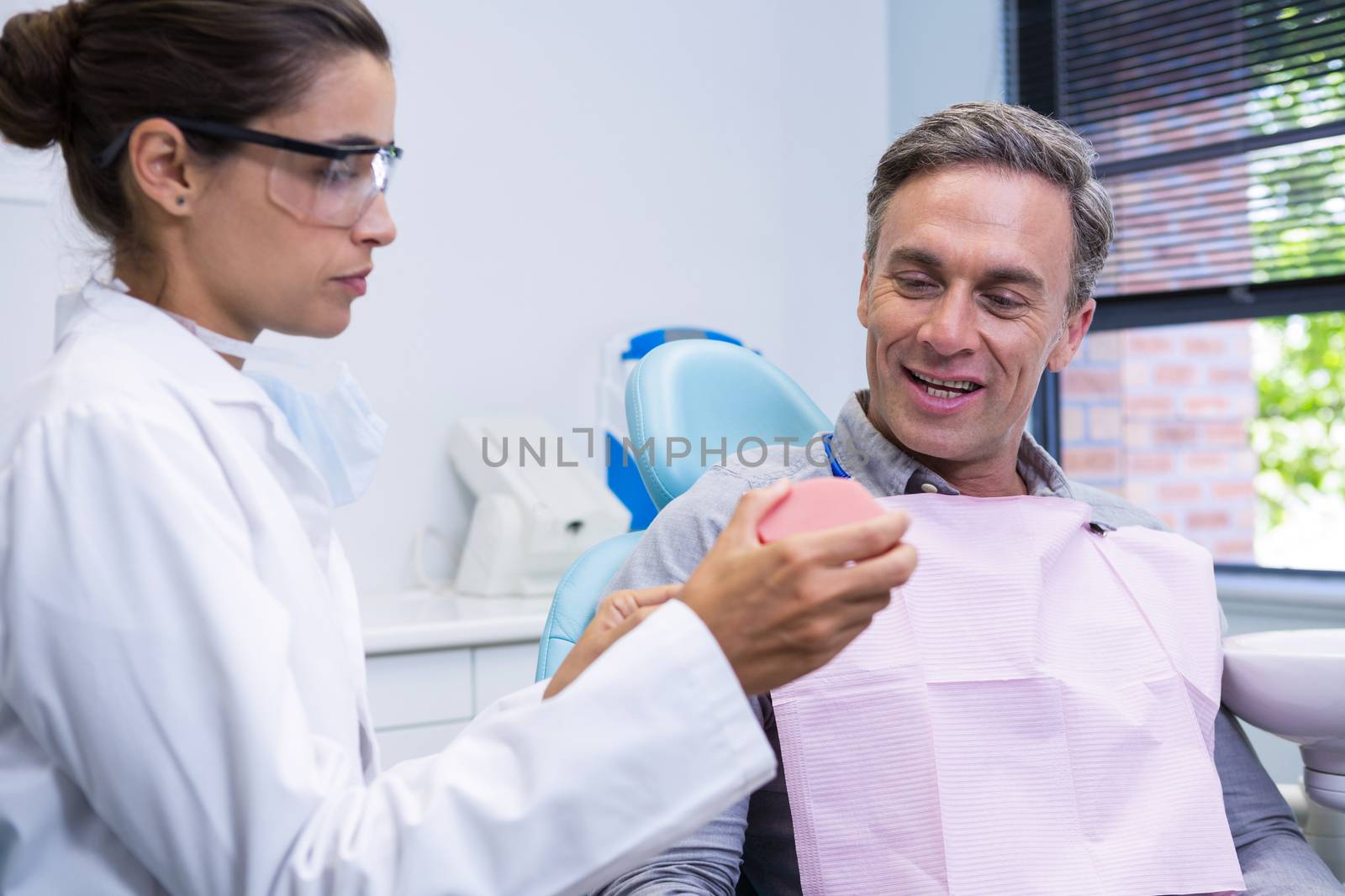 Dentist showing dental mold to man by Wavebreakmedia