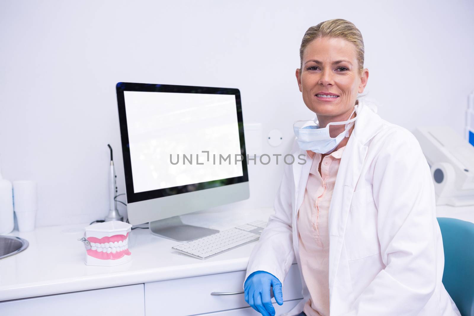 Dentist working while sitting by computer at medical clinic by Wavebreakmedia