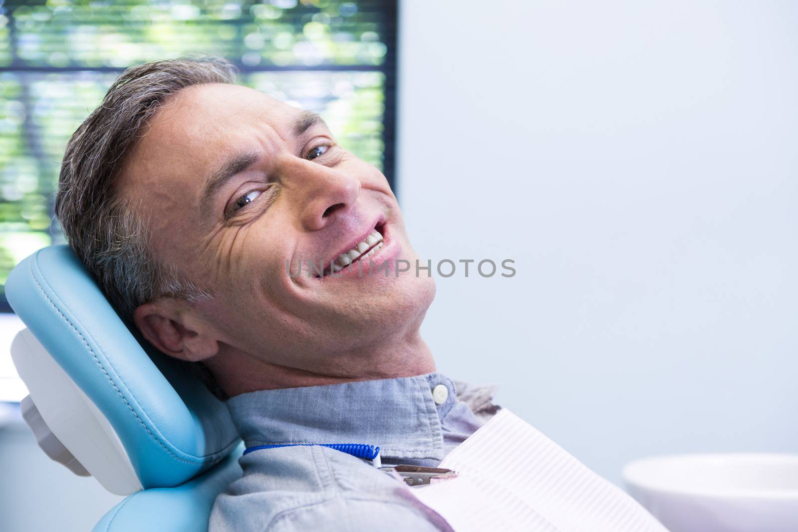 Portrait of smiling man sitting on chair at dentist clinic