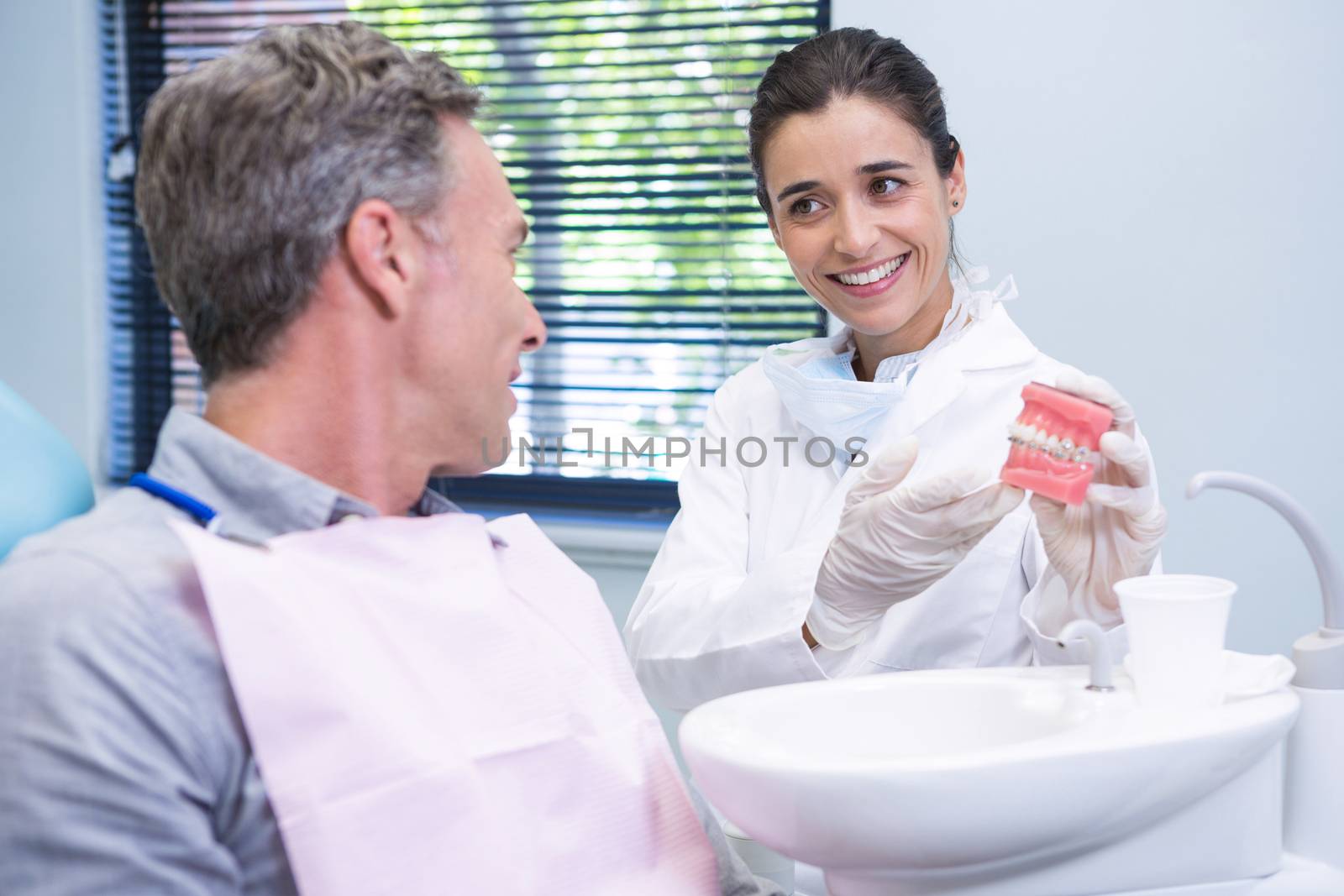 Happy dentist showing dental mold to man at clinic