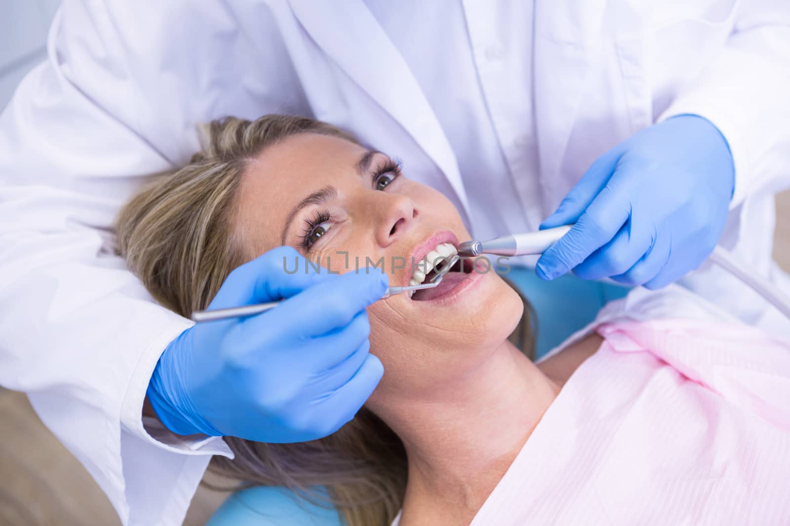 Dentist holding angled mirror while treating woman at medical clinic by Wavebreakmedia