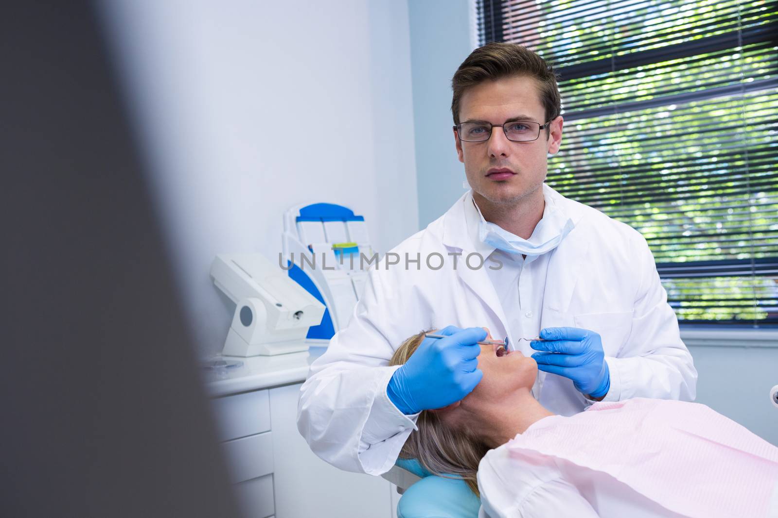 Portrait of dentist cleaning woman teeth while standing against wall at dental clinic