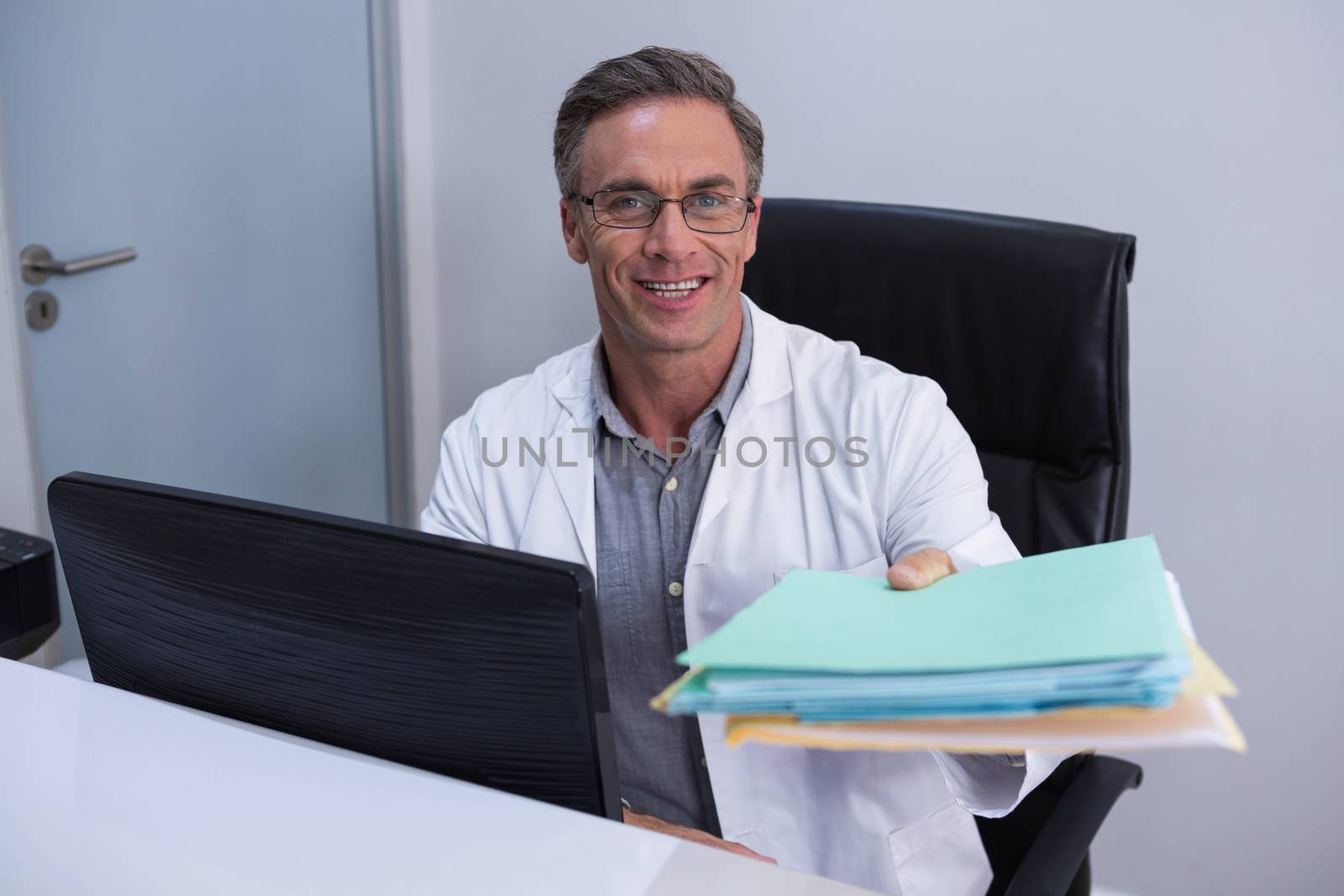 Portrait of dentist holding file while sitting by computer in clinic