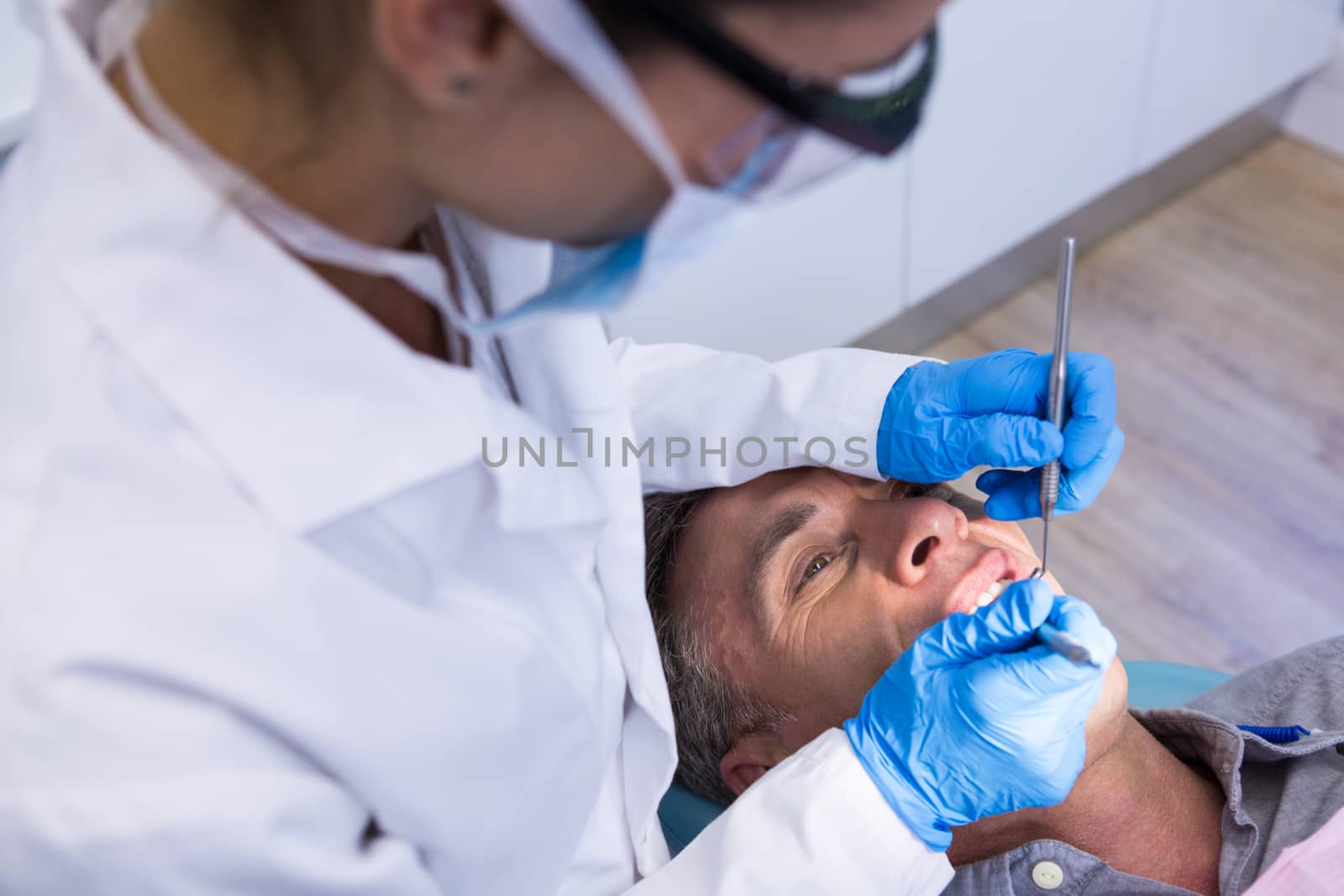 High angle view of dentist holding tools while examining man at clinic