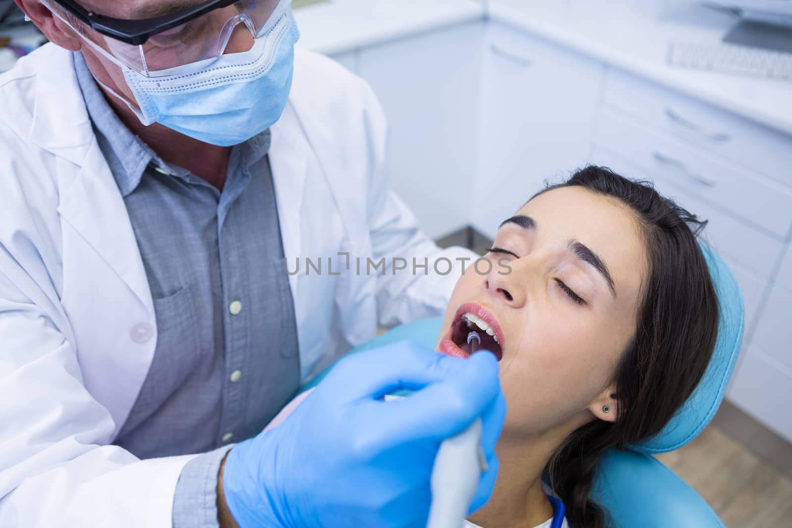 Dentist holding tools while treating woman at medical clinic by Wavebreakmedia